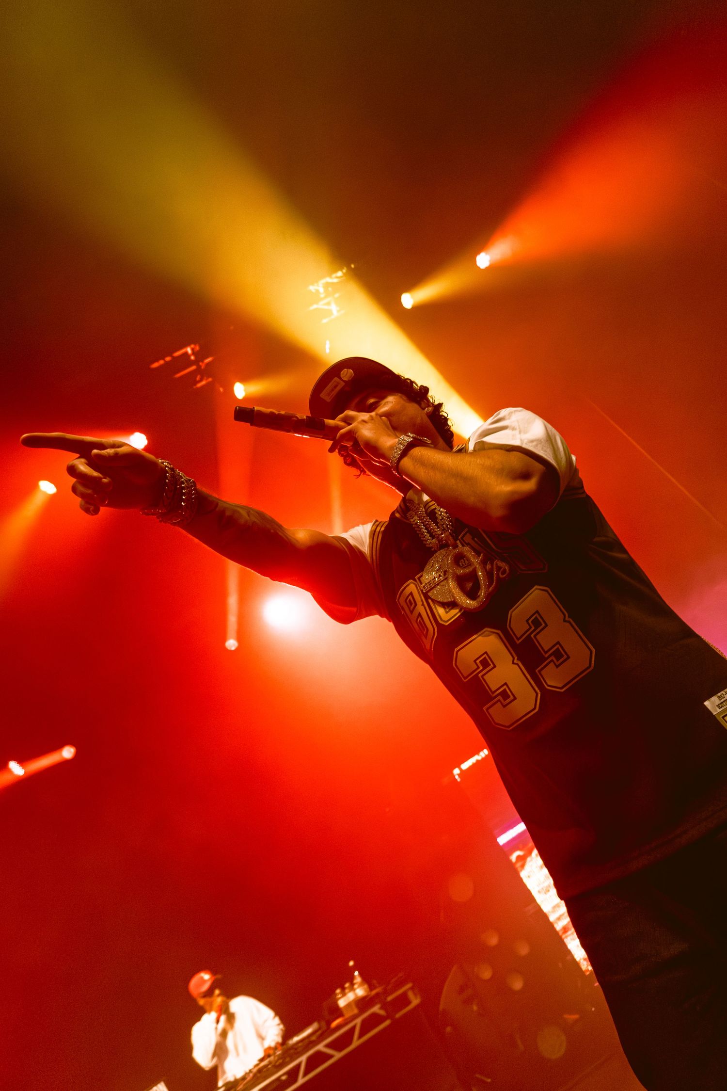 Hip hop artist performs energetically under dramatic red and yellow stage lighting.