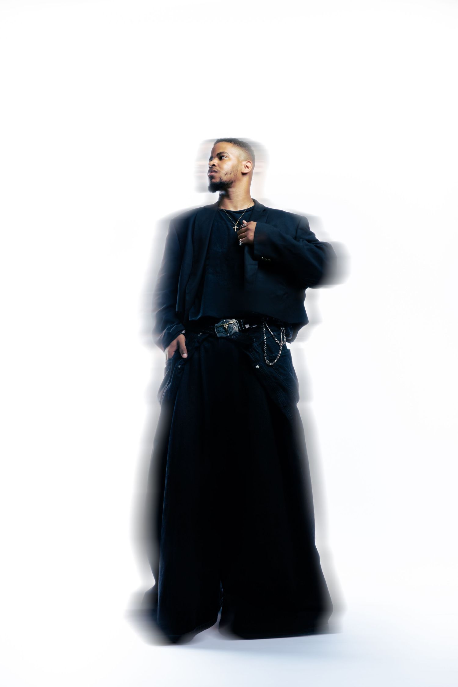 Artistic high-key portrait of a person wearing oversized black clothing against white background.