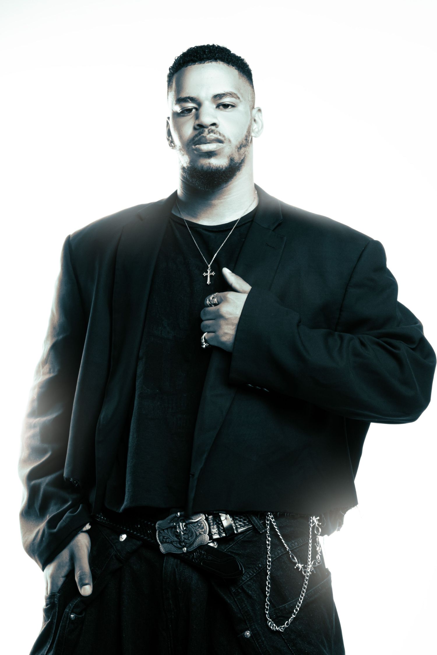 Professional studio portrait of a person in all black attire with a chain belt against white background.