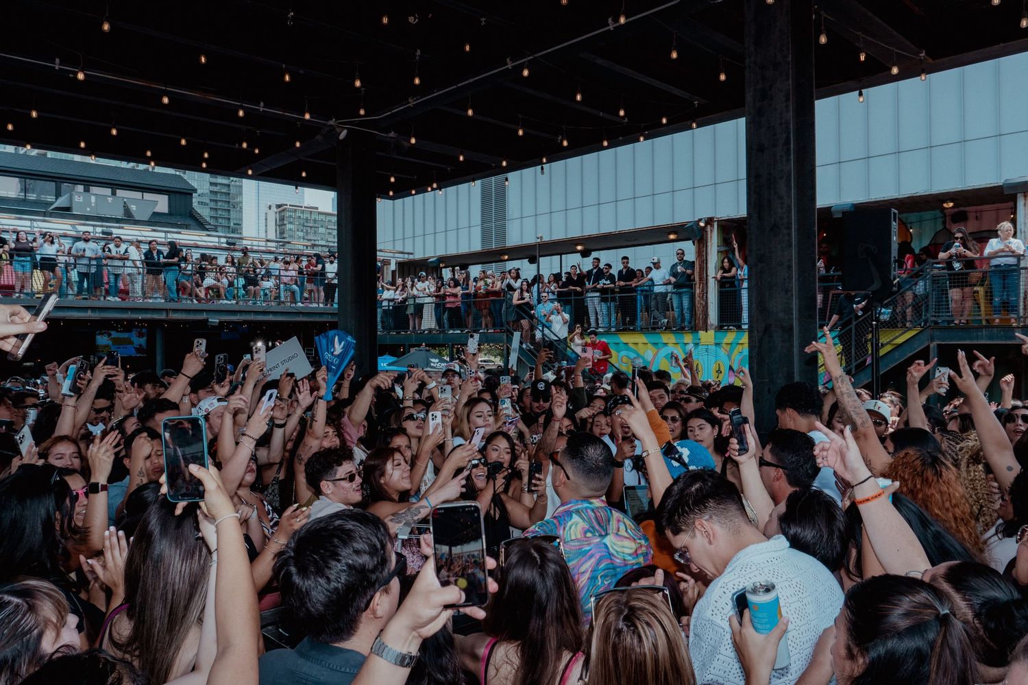 Crowd with raised hands at a nighttime concert under starlit ceiling.
