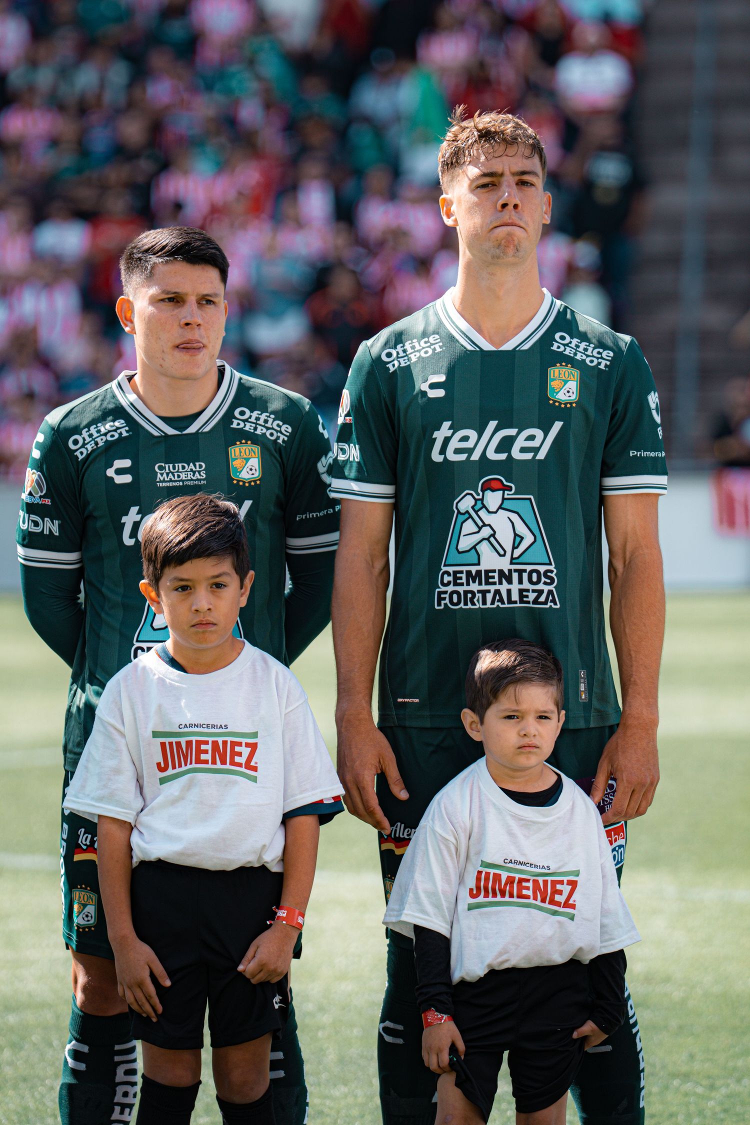 Youth soccer players line up on field wearing green jerseys and white escort uniforms.