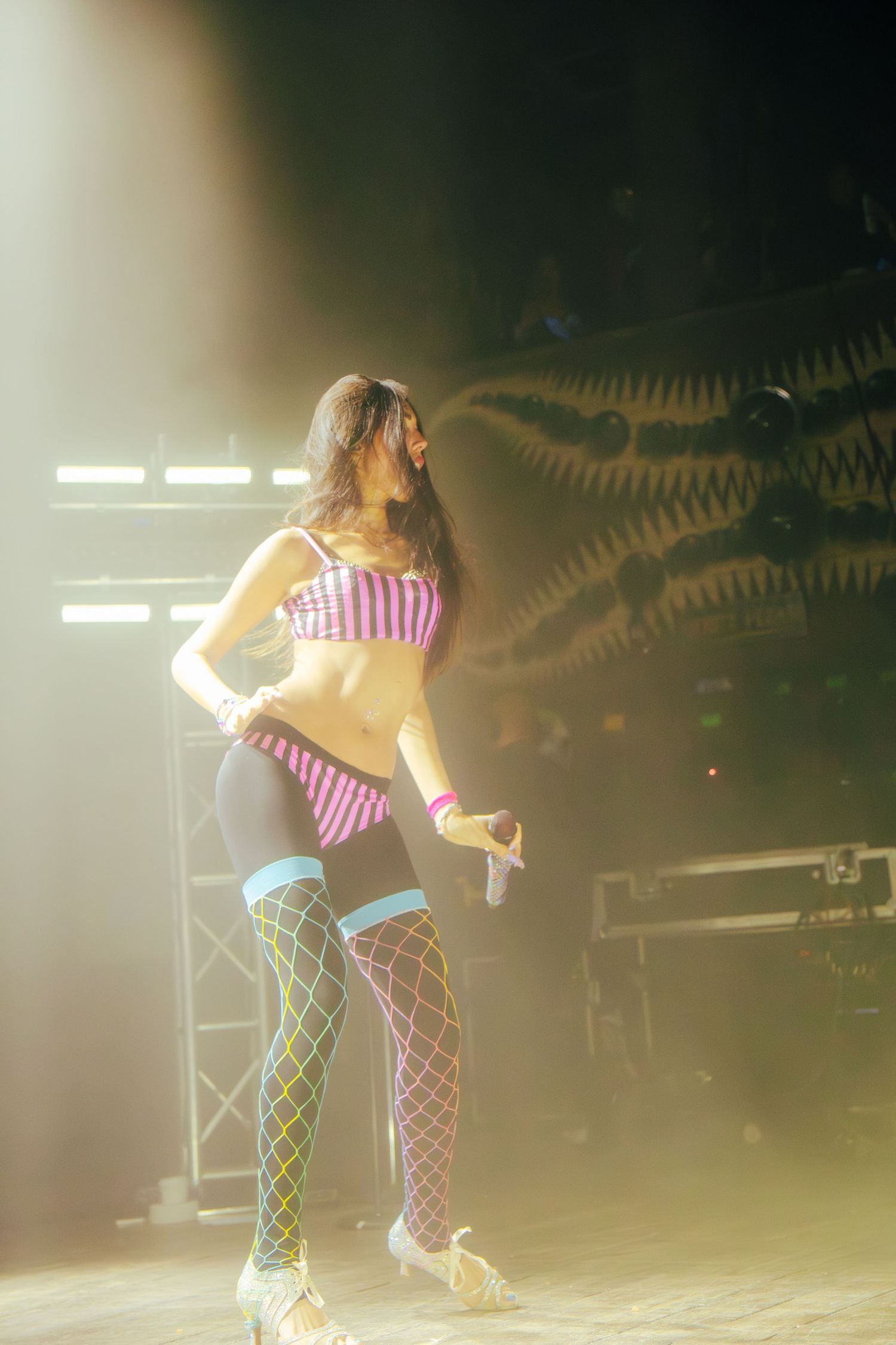 A dancer performs on stage in fishnet stockings and red and white striped top under dramatic lighting.