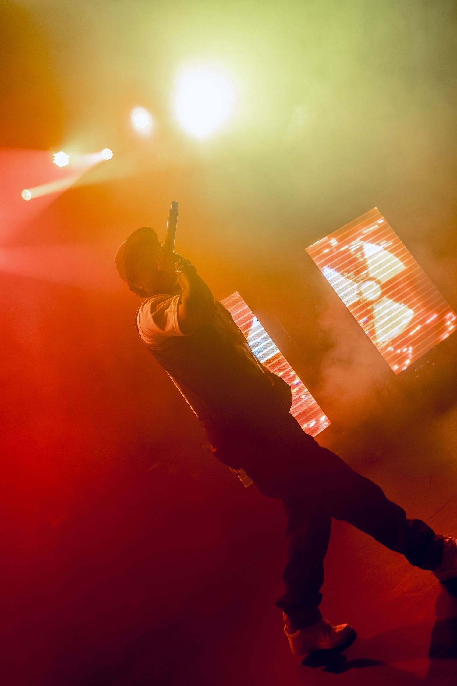 Performer in silhouette strikes dynamic pose against colorful concert lighting and LED screen.
