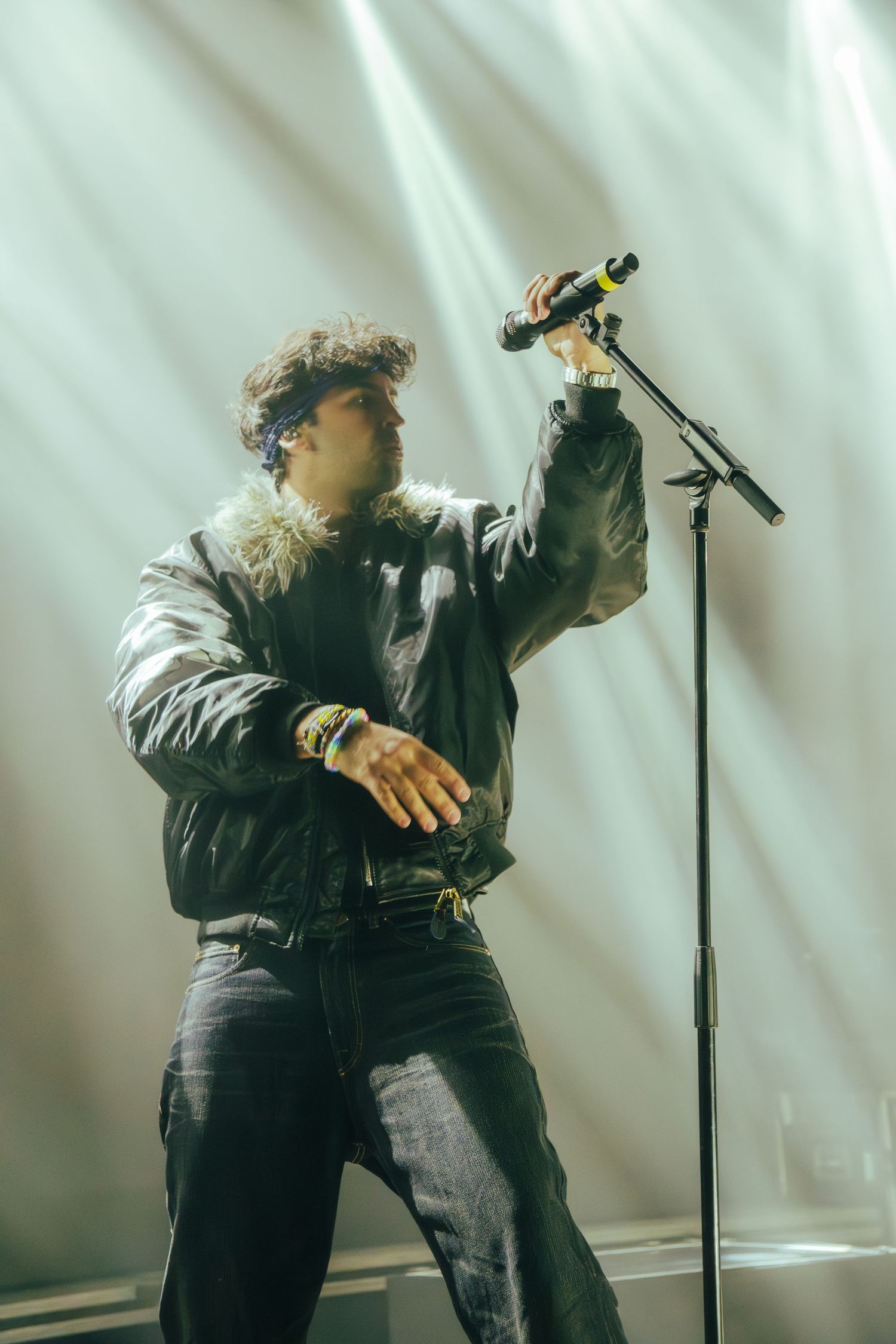 A dramatic silhouetted performer gestures passionately on stage with a microphone stand against bright backlighting.