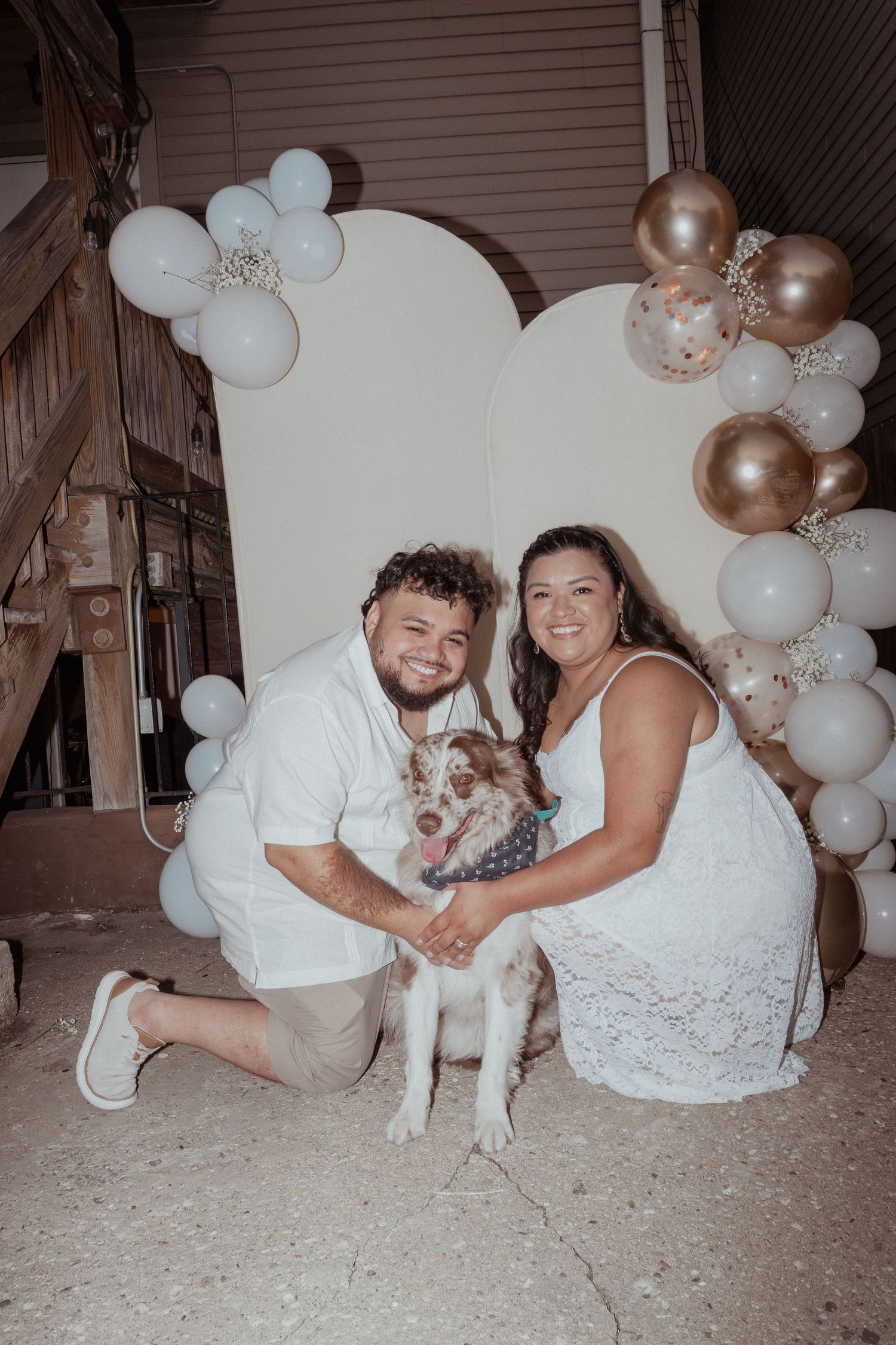 Wedding couple posing with their white dog against balloon decorations.
