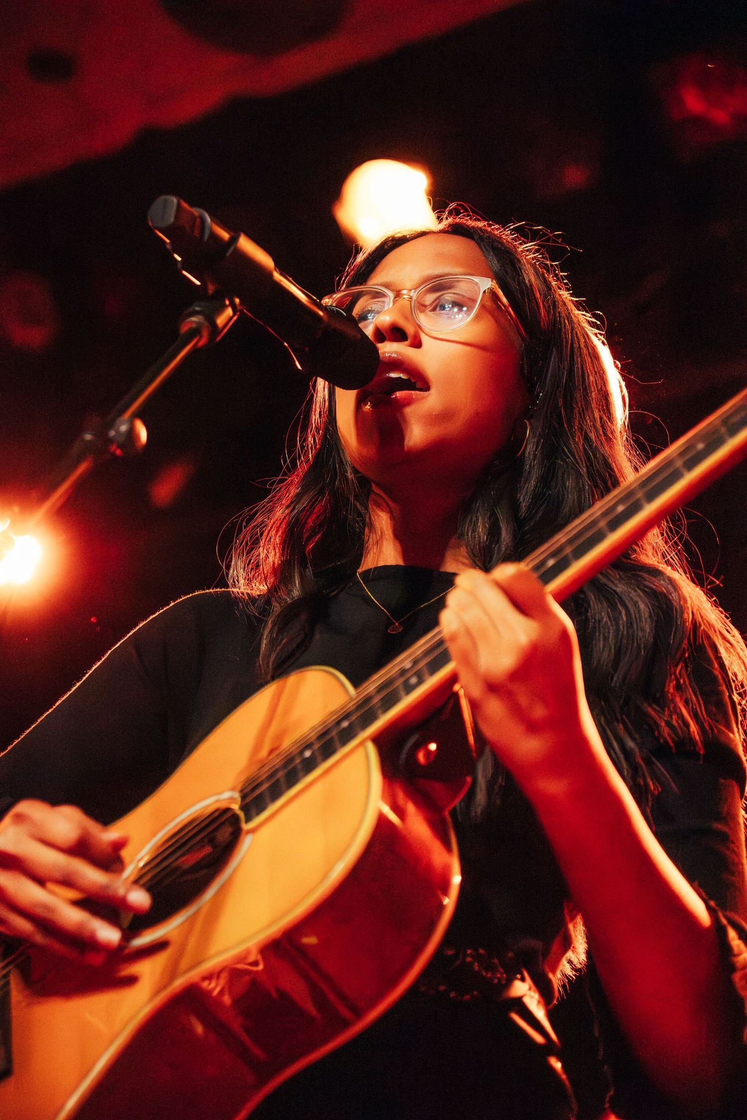 A musician performs passionately on an acoustic guitar under dramatic red stage lighting.