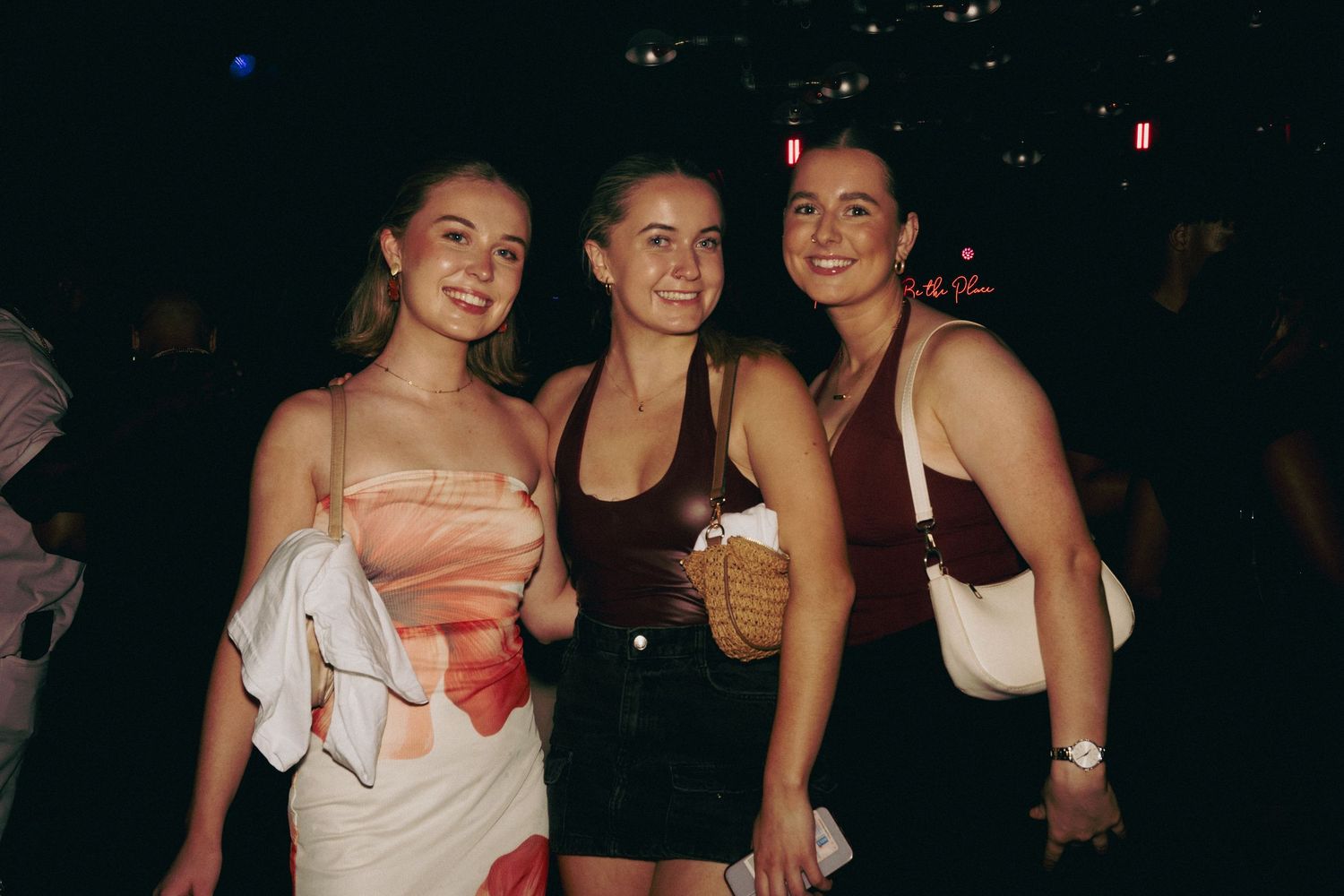 Group of friends smiling together at a social gathering in dark lighting.