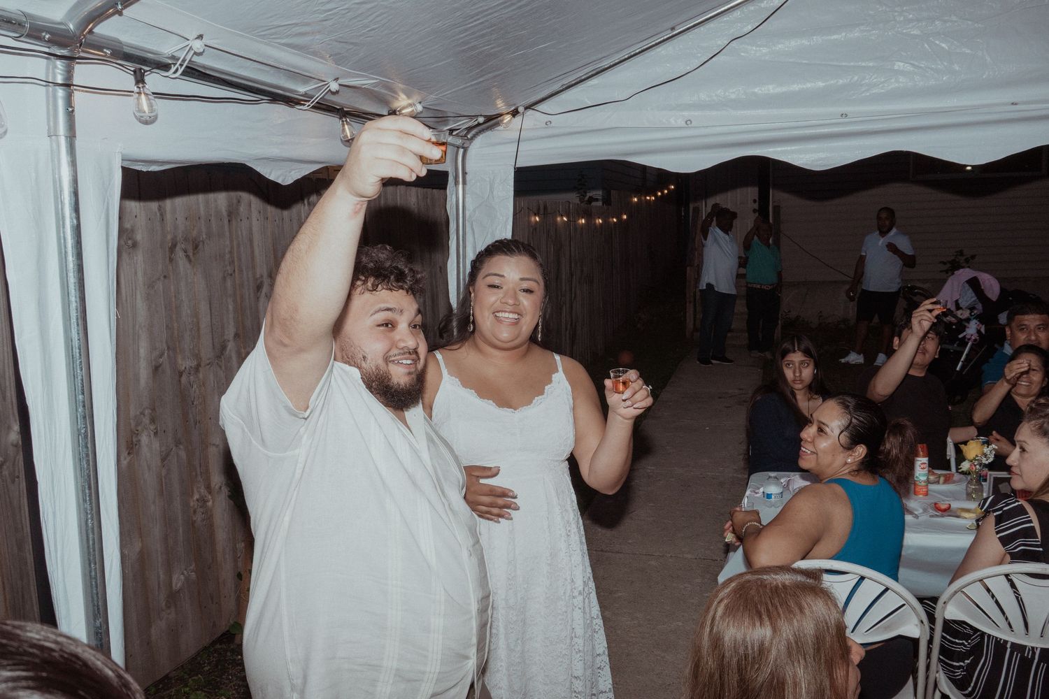 Wedding reception dance scene under white tent with guests in background.