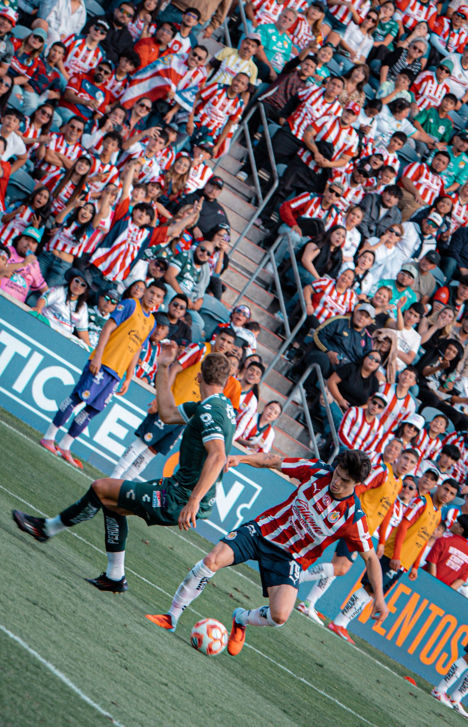 Soccer match action shot with players and crowd visible in stadium background.