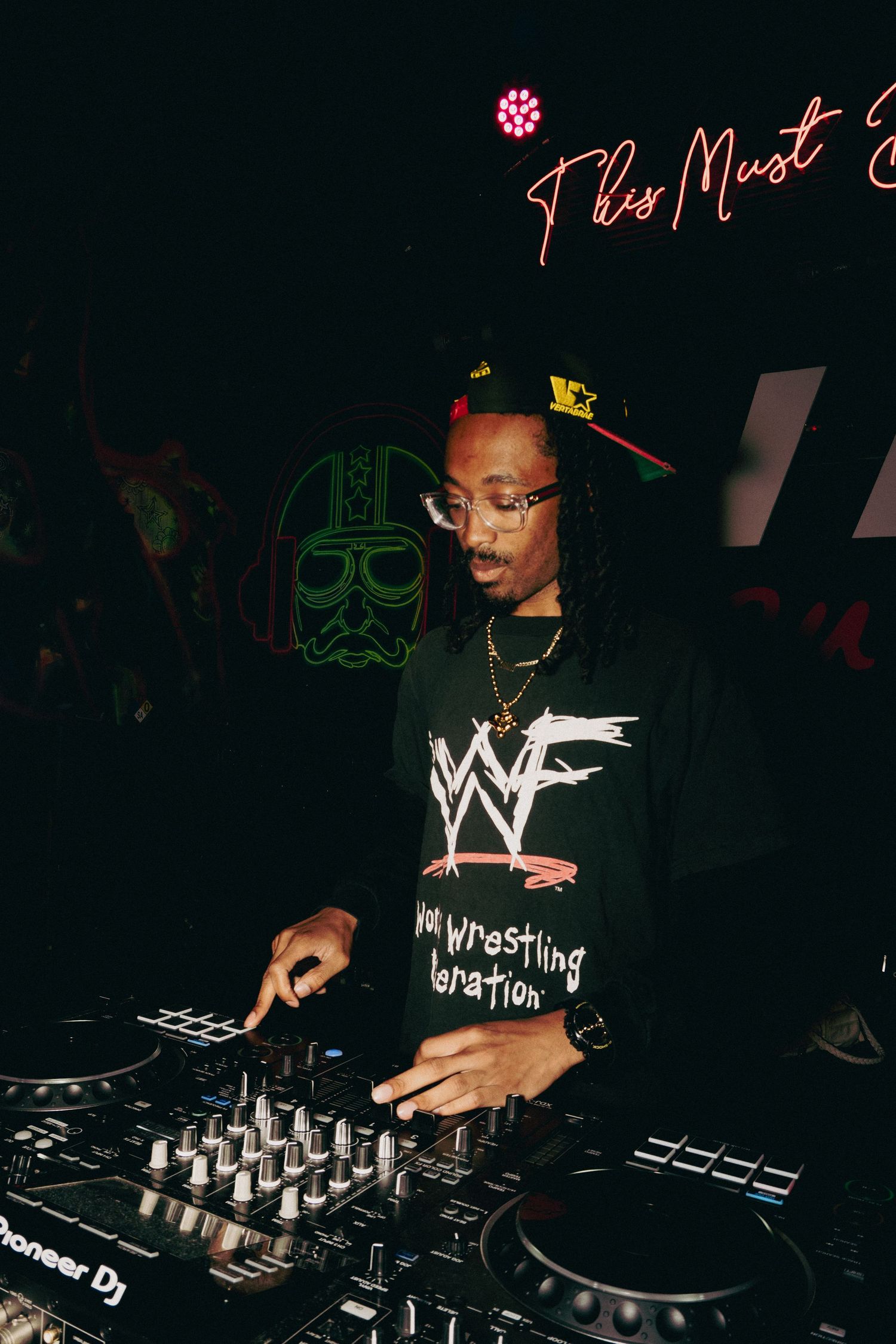 DJ performing at nightclub wearing wrestling-themed shirt.