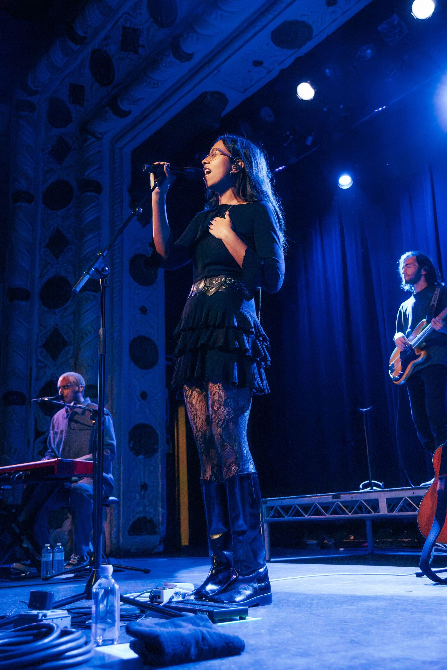 Musicians perform on stage with dramatic blue lighting and minimal staging during a live concert performance.