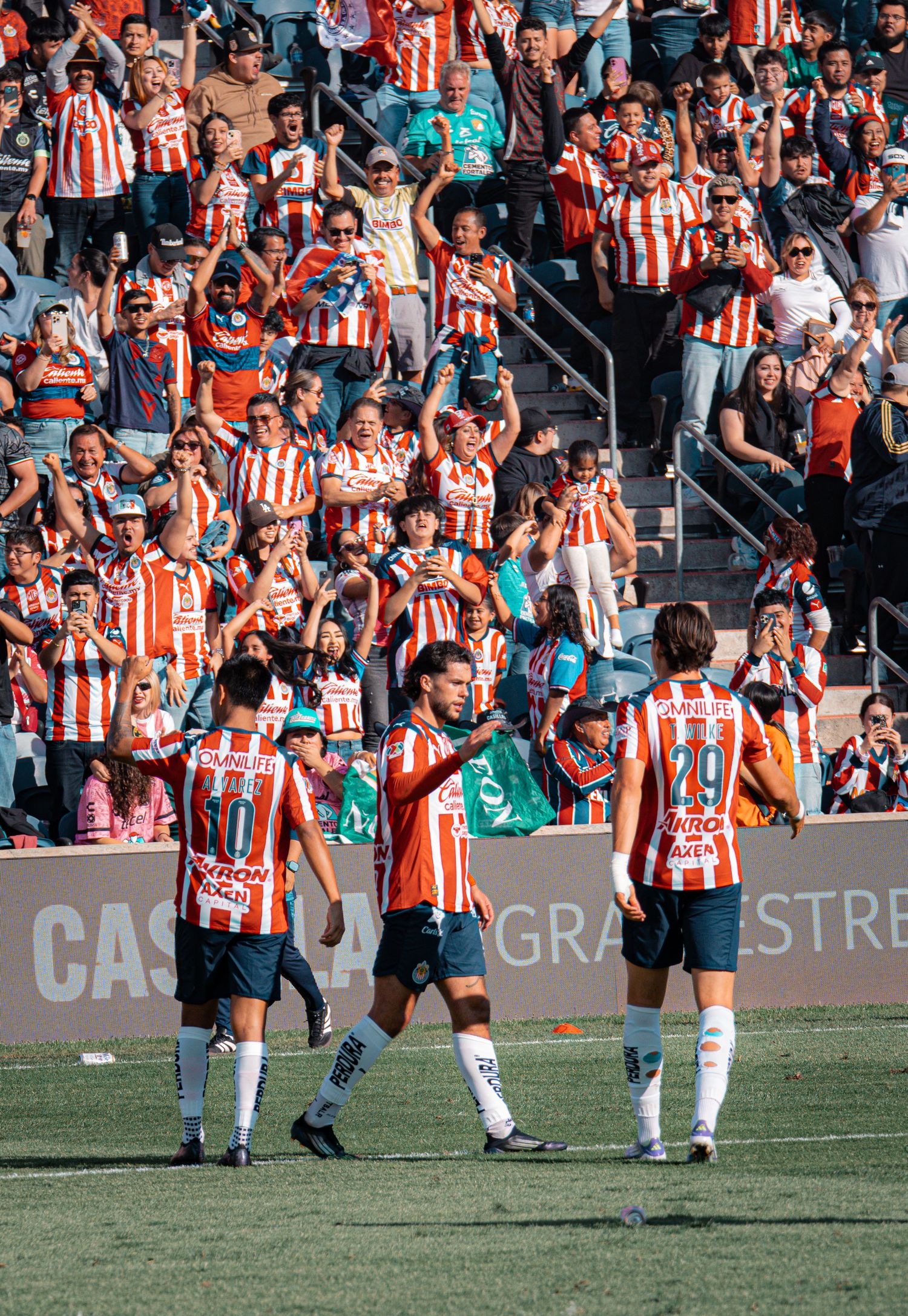 Soccer team celebrates with fans in stadium stands wearing red and white striped jerseys.