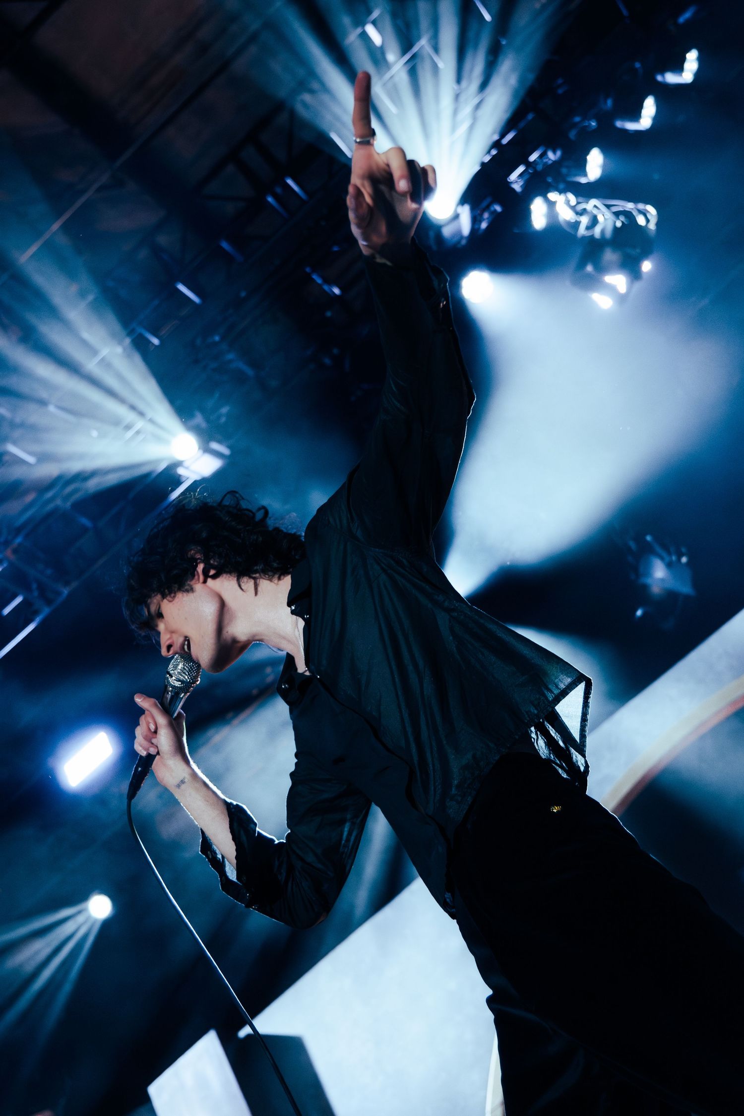 Silhouetted performer on stage illuminated by dramatic blue and white spotlights during an energetic concert performance.