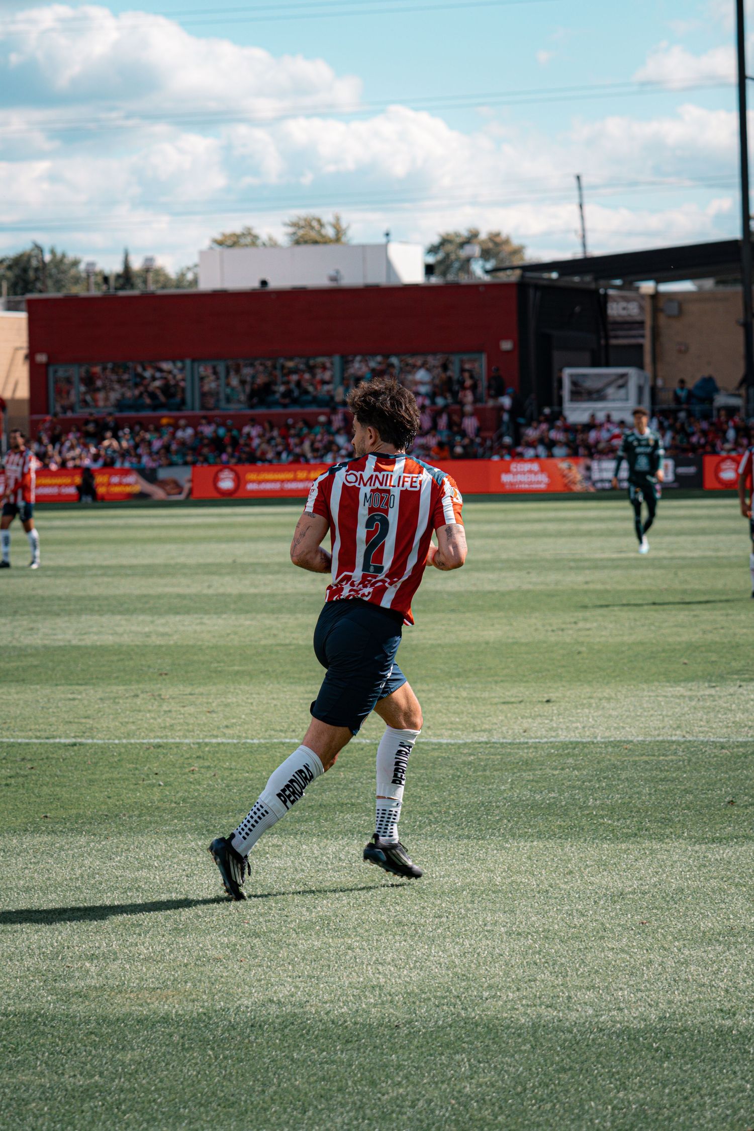 Soccer players in action on a green turf field during a sunny day match.