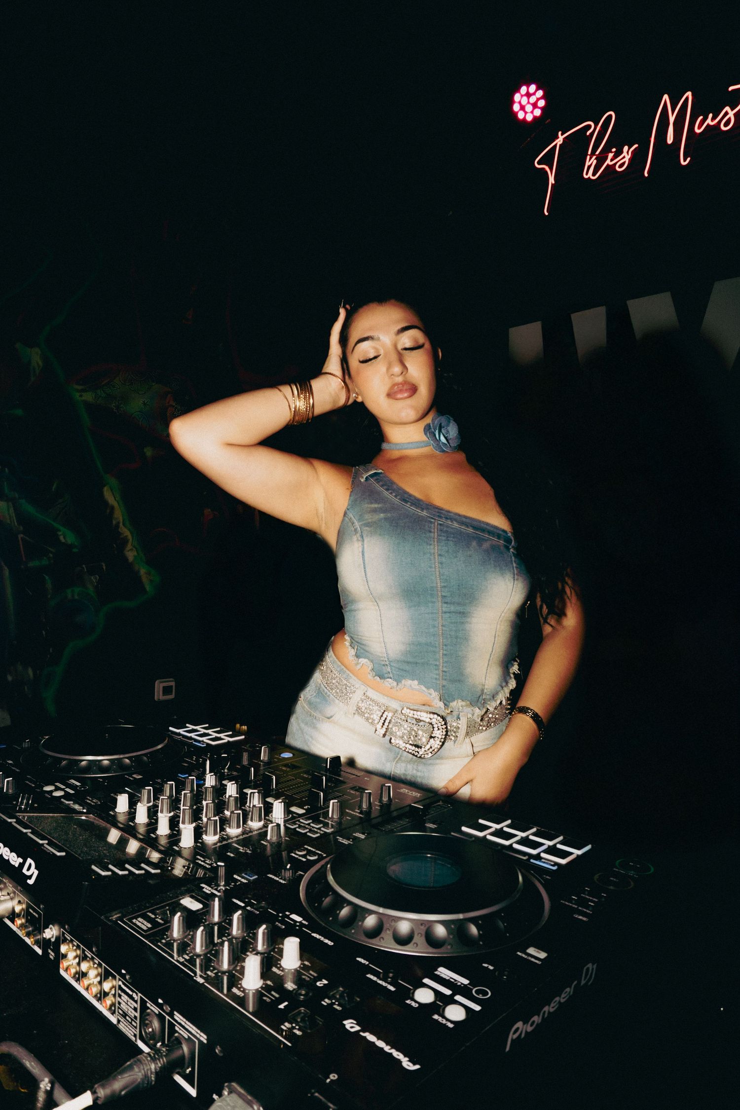 DJ performing on professional equipment in dark nightclub setting.