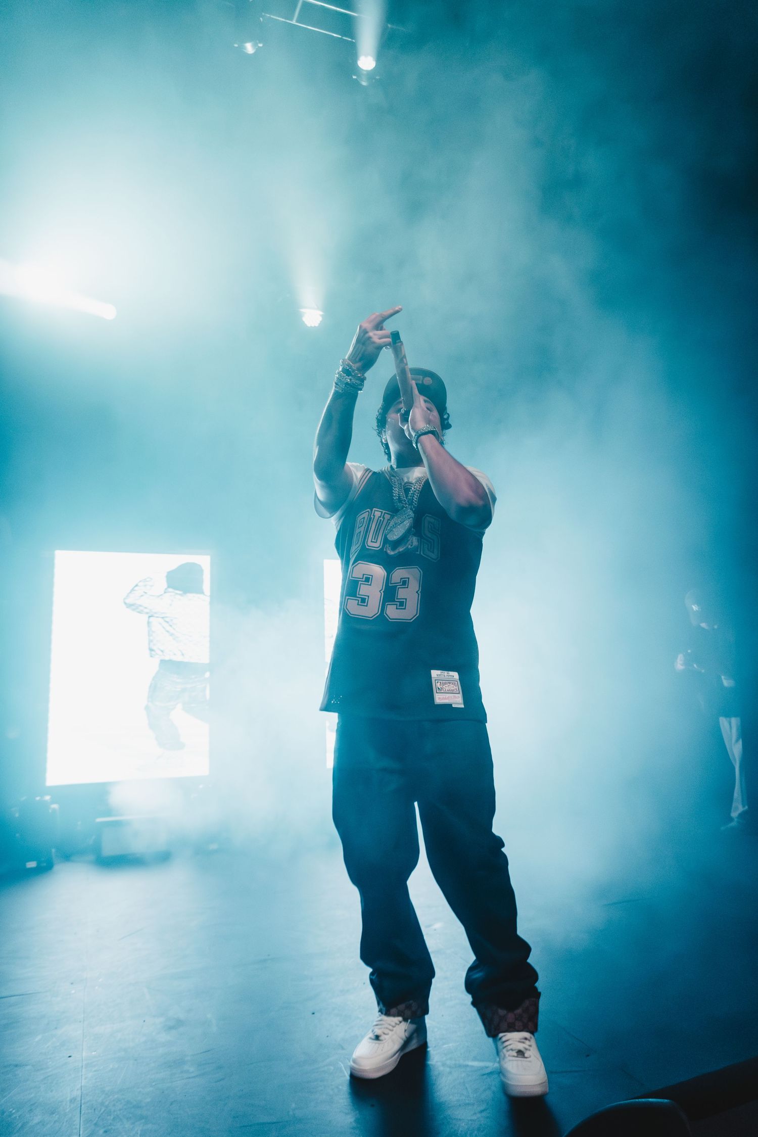 Silhouette of performer in sports jersey on stage surrounded by blue smoke effects.