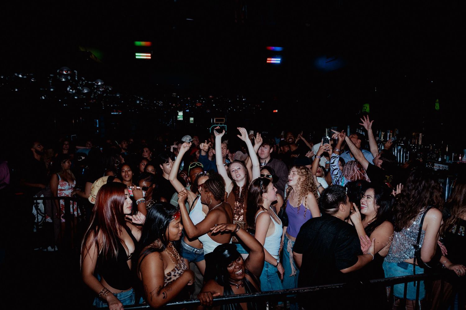 Crowded nightclub dance floor with people raising hands in celebration.