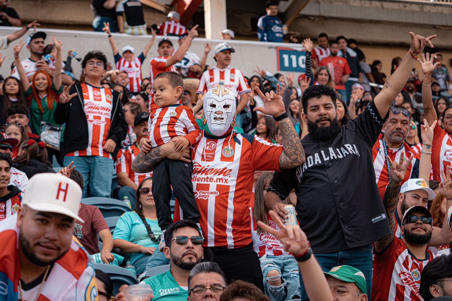 Excited soccer fans in red and white jerseys cheer from the stadium stands.