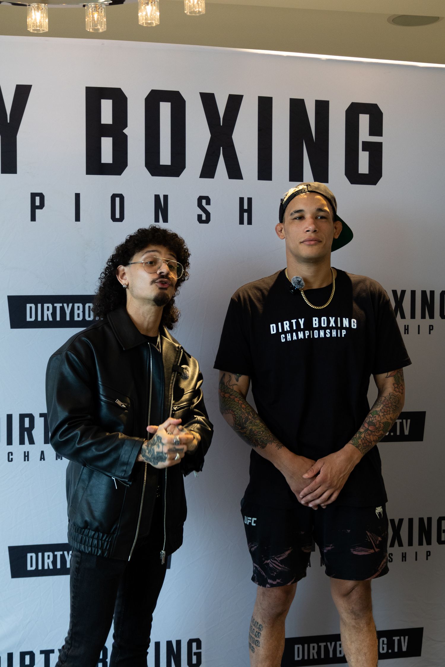 Group wearing black clothing poses against boxing championship backdrop with overhead lighting.