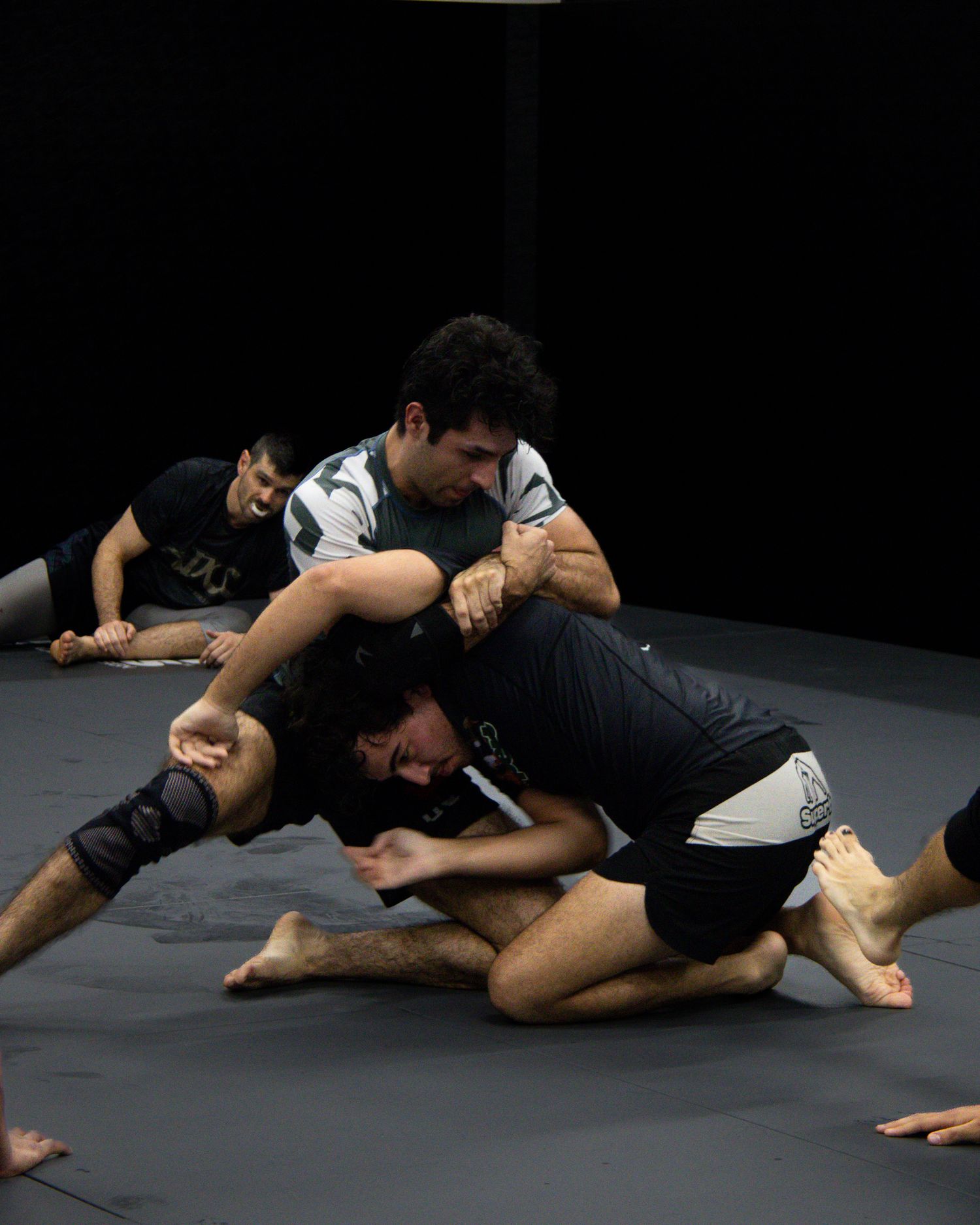 Two martial artists demonstrating grappling techniques on a black mat in a sequence of moves.