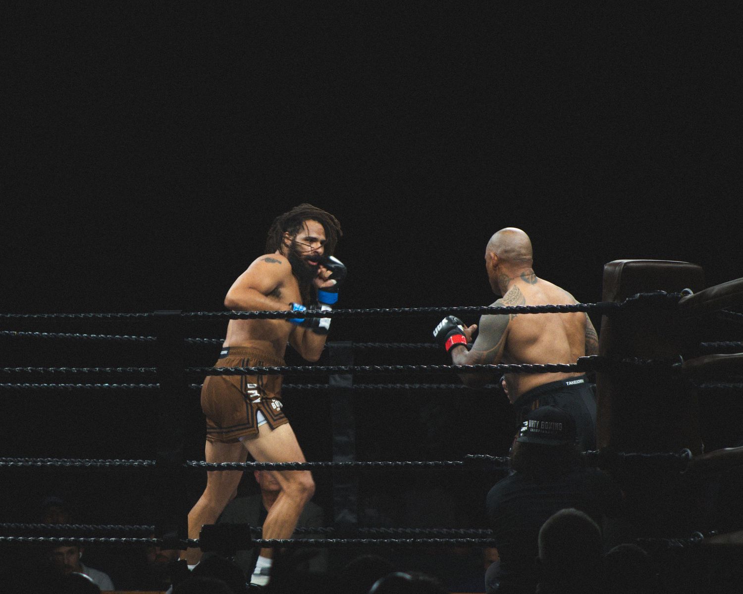 Professional boxers trade punches during a competitive match in a dark arena.