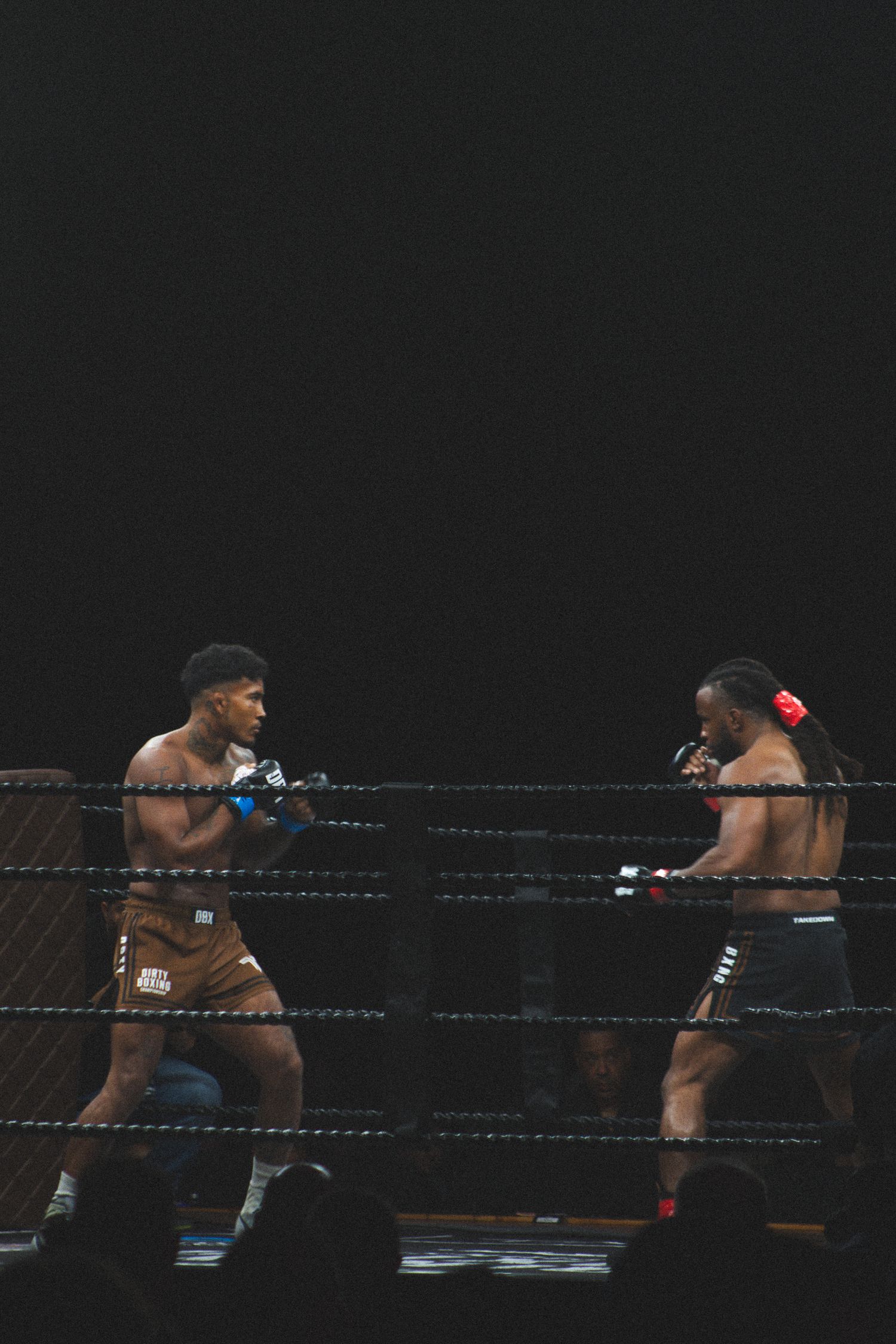 Two boxers square up in fighting positions during a professional match under dramatic lighting.
