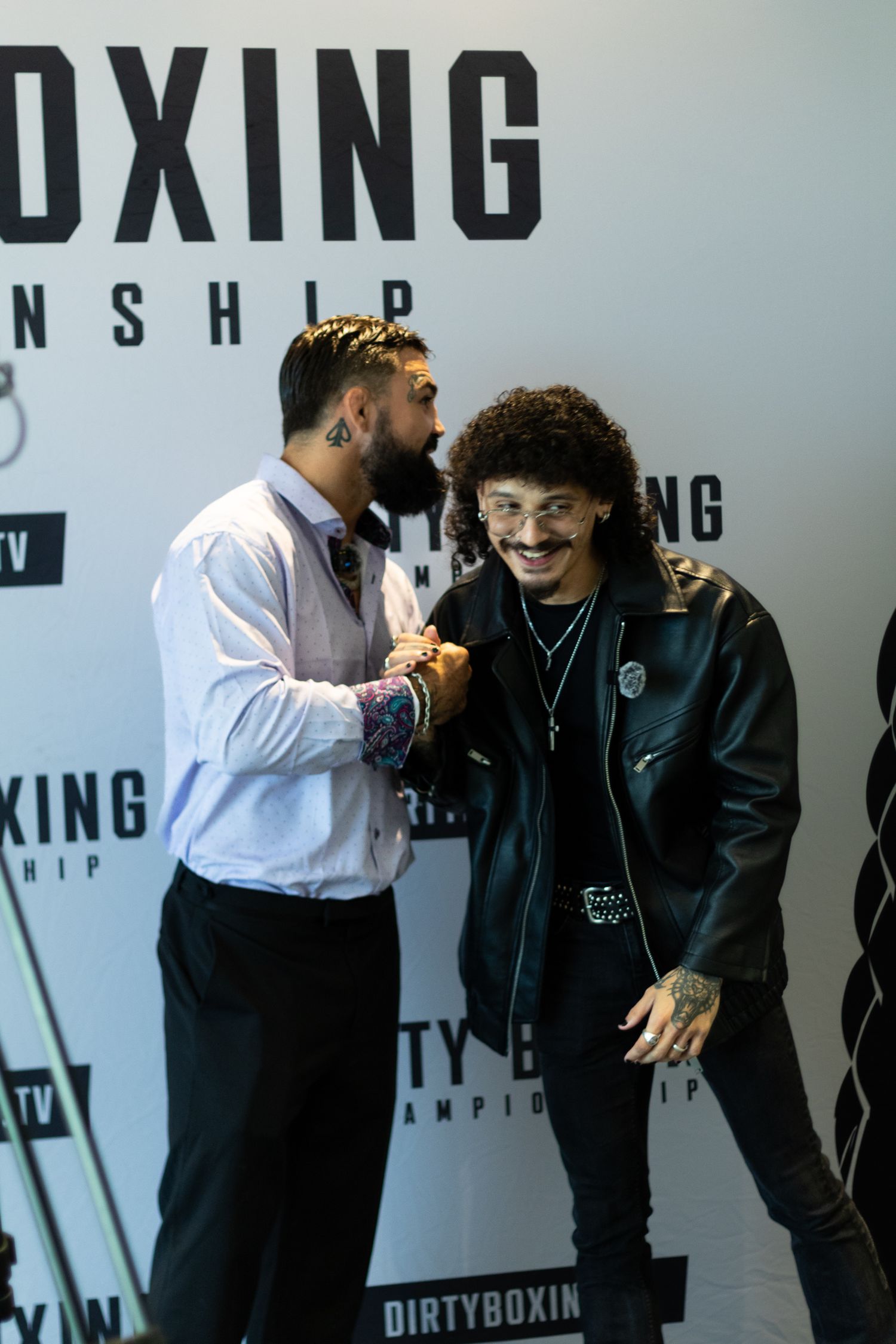 Two people having an animated conversation in front of boxing event backdrop.