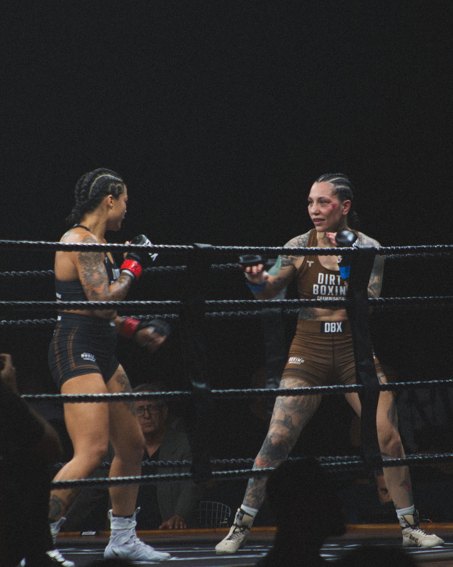 Two boxers exchange punches during an intense match in a dimly lit boxing ring.