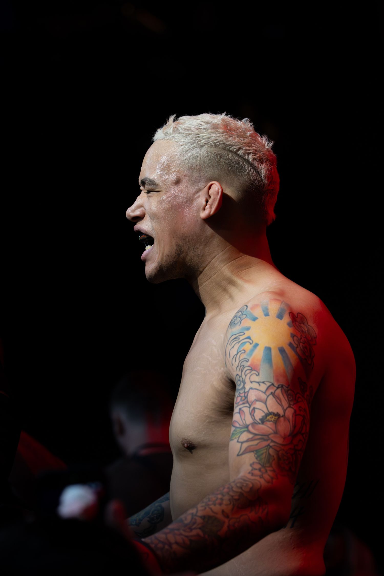 A tattooed fighter shown in profile under dramatic lighting.