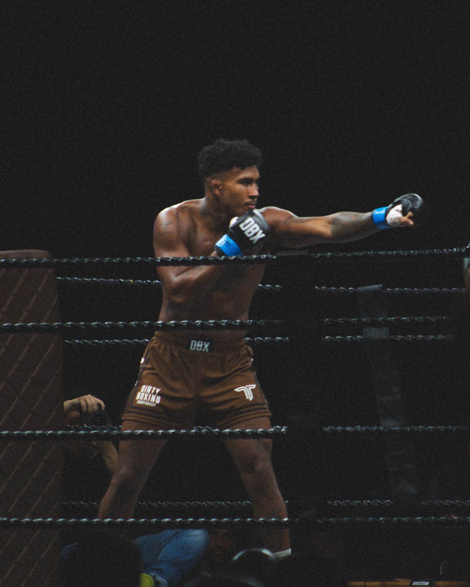 A boxer in brown trunks launches an aggressive attack in the ring.