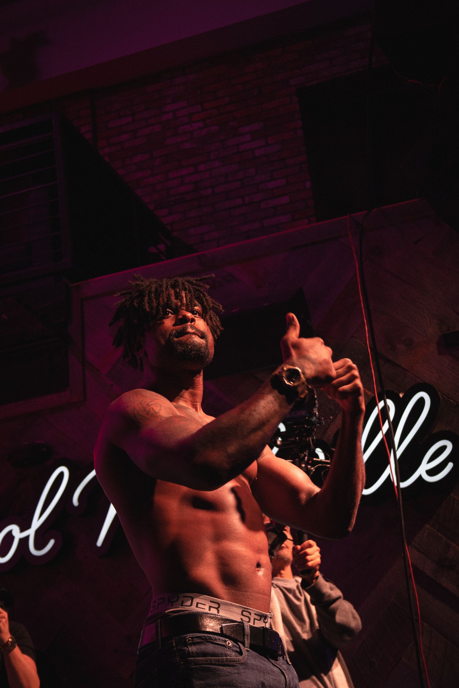 Performer sings passionately on dimly lit stage with neon signage in background.