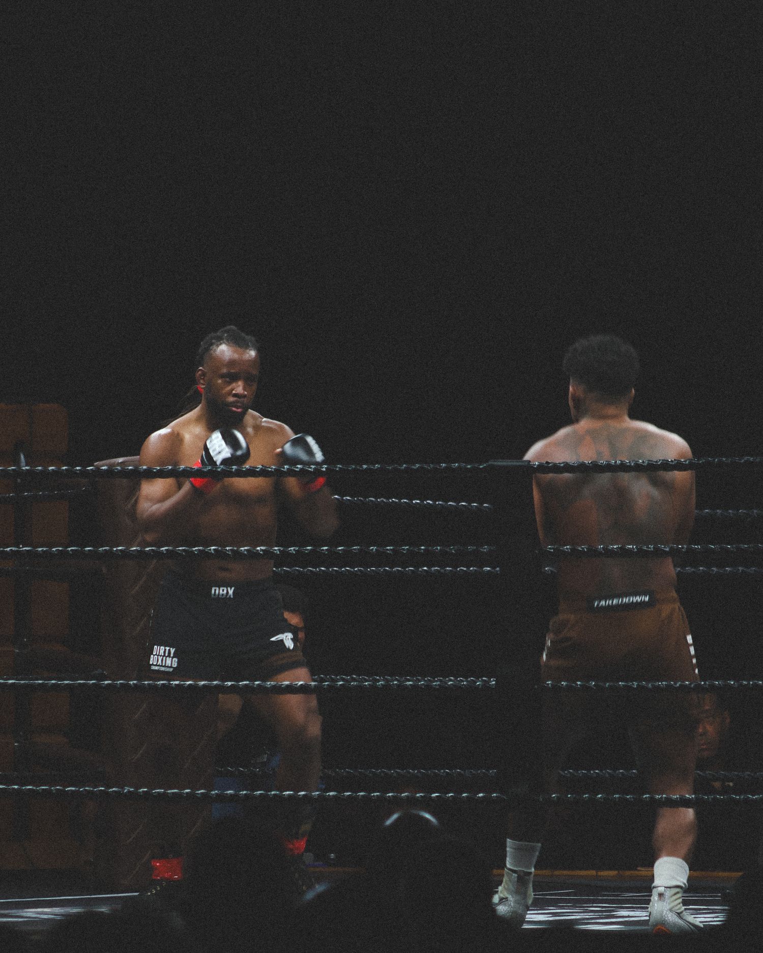 Two boxers face off in fighting stances during a professional match in a darkened arena.
