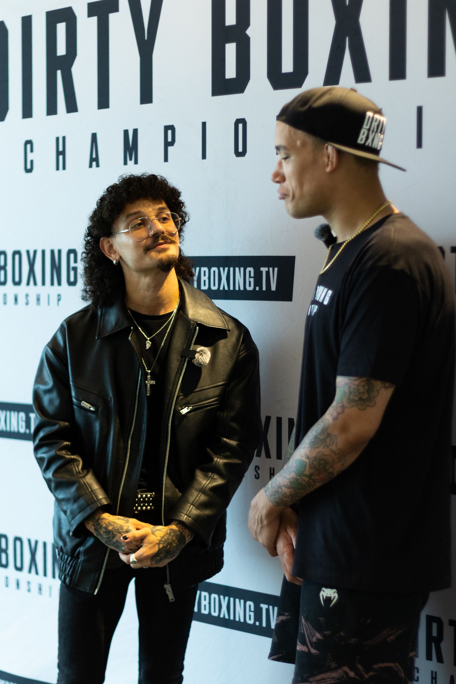 Two people engaged in conversation against boxing event backdrop.