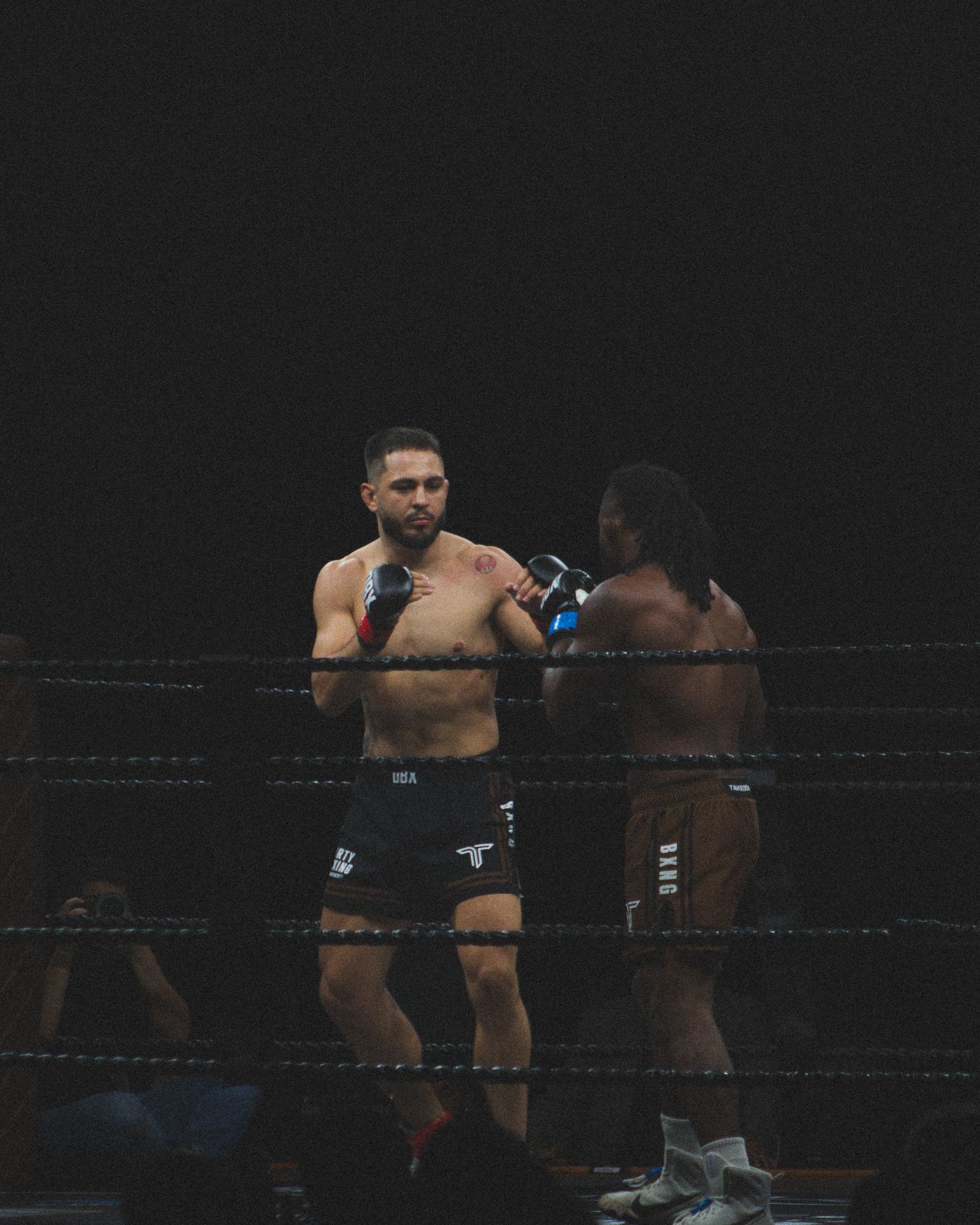 Athletes trade punches during an intense boxing match in low light conditions.