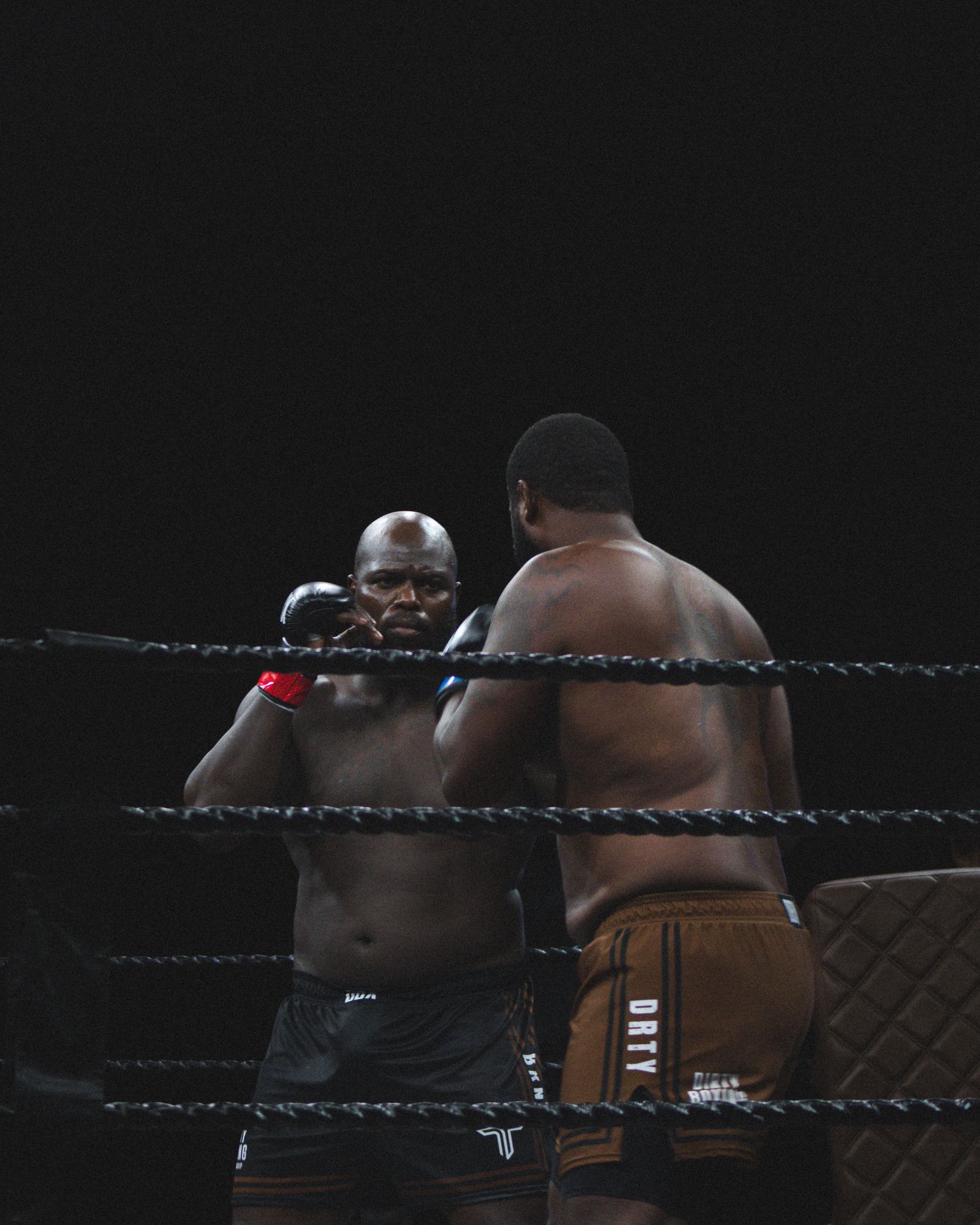 Two boxers engage in close combat within the ropes of a professional boxing ring.