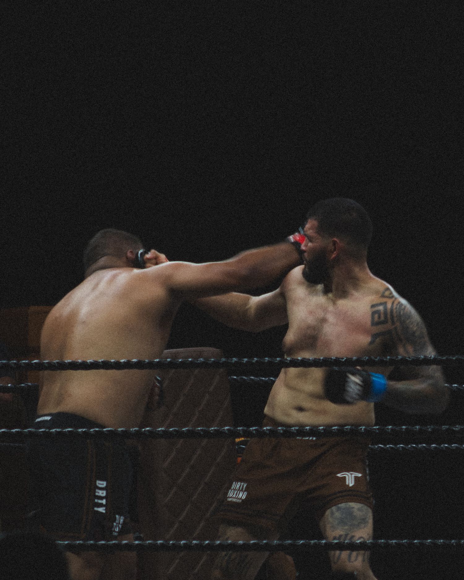 Two boxers exchange punches in a dramatic moment during a professional boxing match in a dark arena.