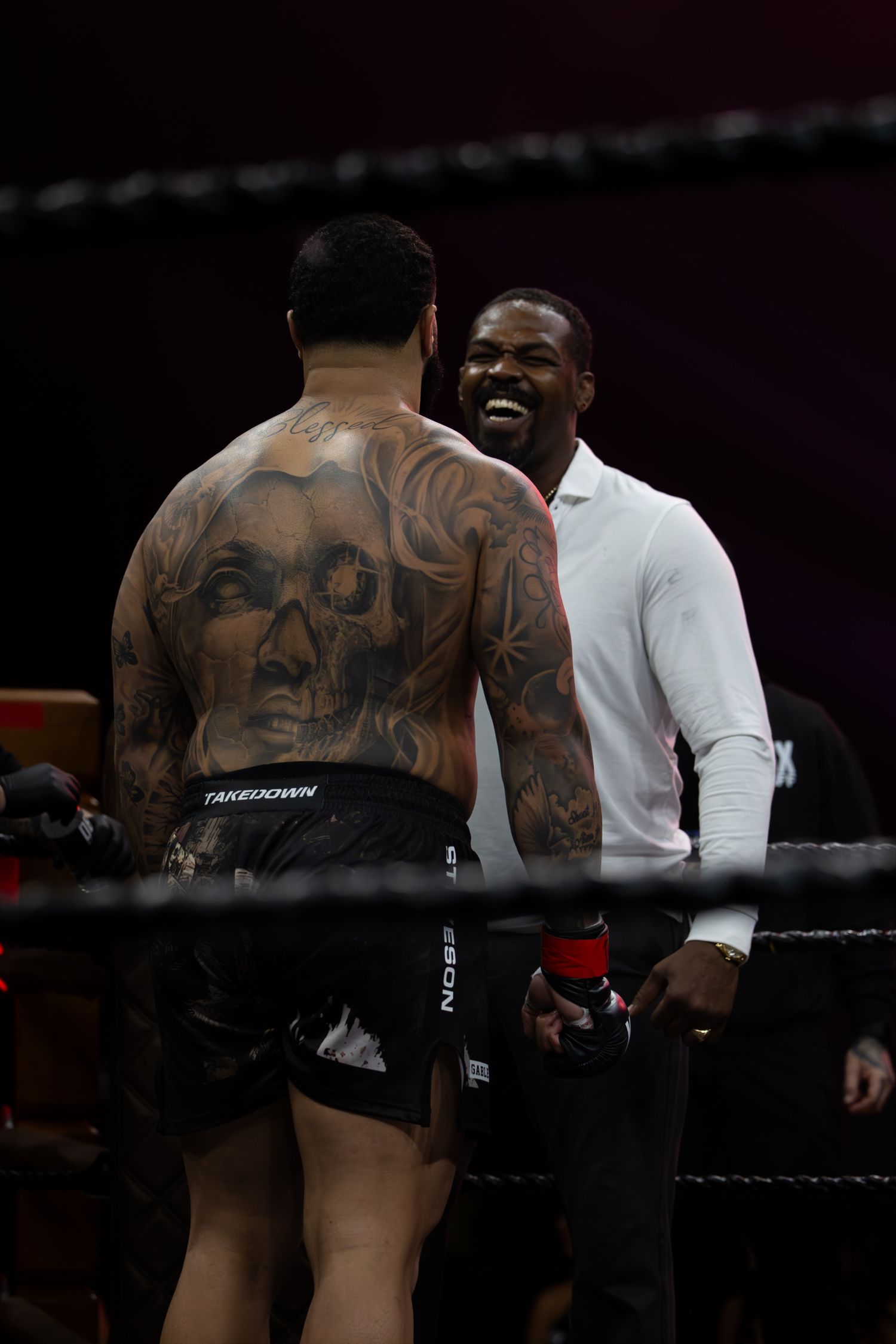 Performer with intricate back tattoos stands on stage wearing white.
Gable Steveson & Jon Jones