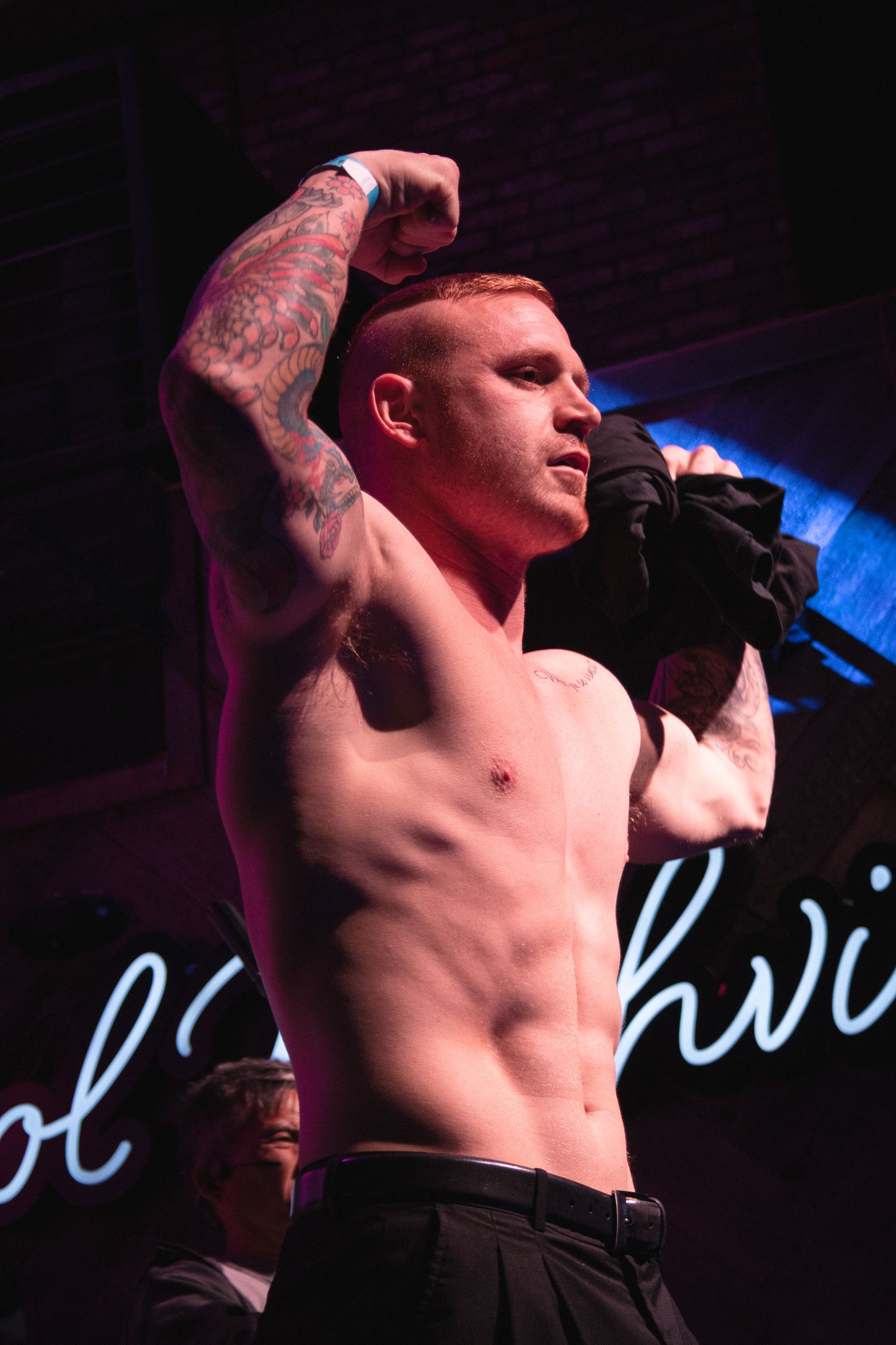 Shirtless performer sings intensely under blue and red stage lighting.