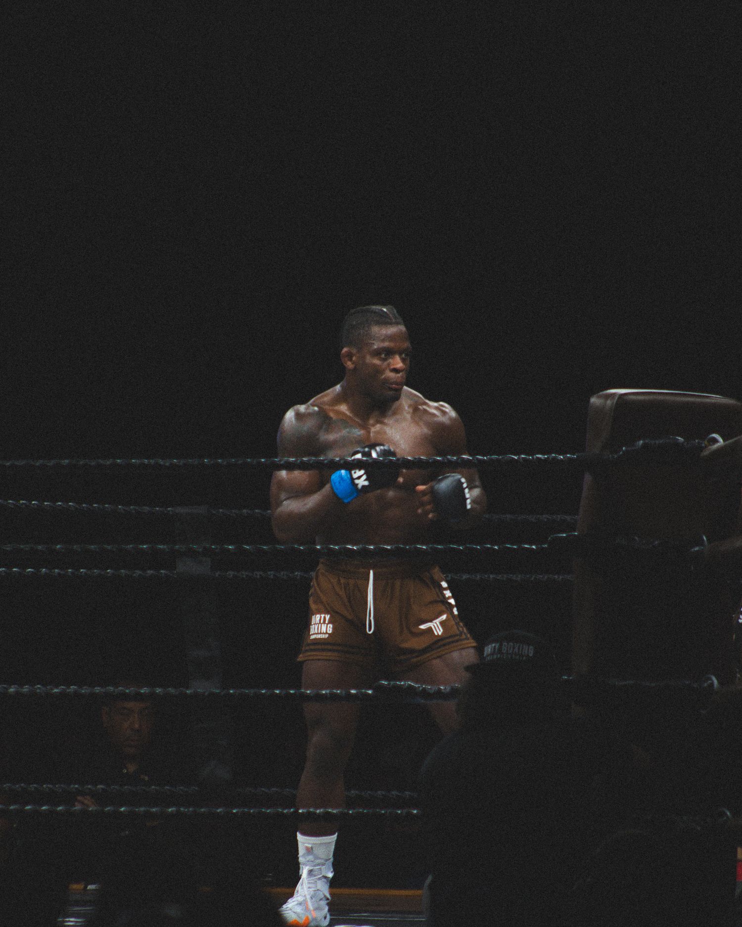 Two fighters exchange punches during an intense boxing match in a darkly lit ring.