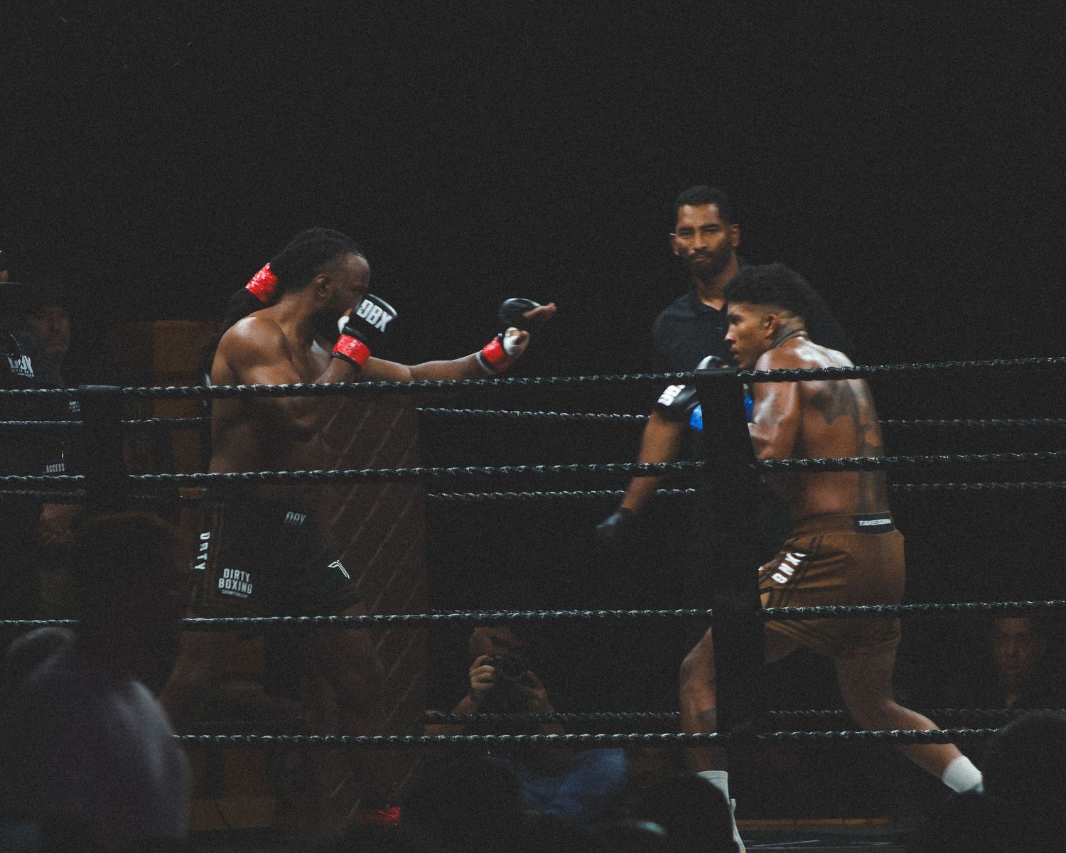 Boxers square off in fighting stance during a professional match in a dark arena.