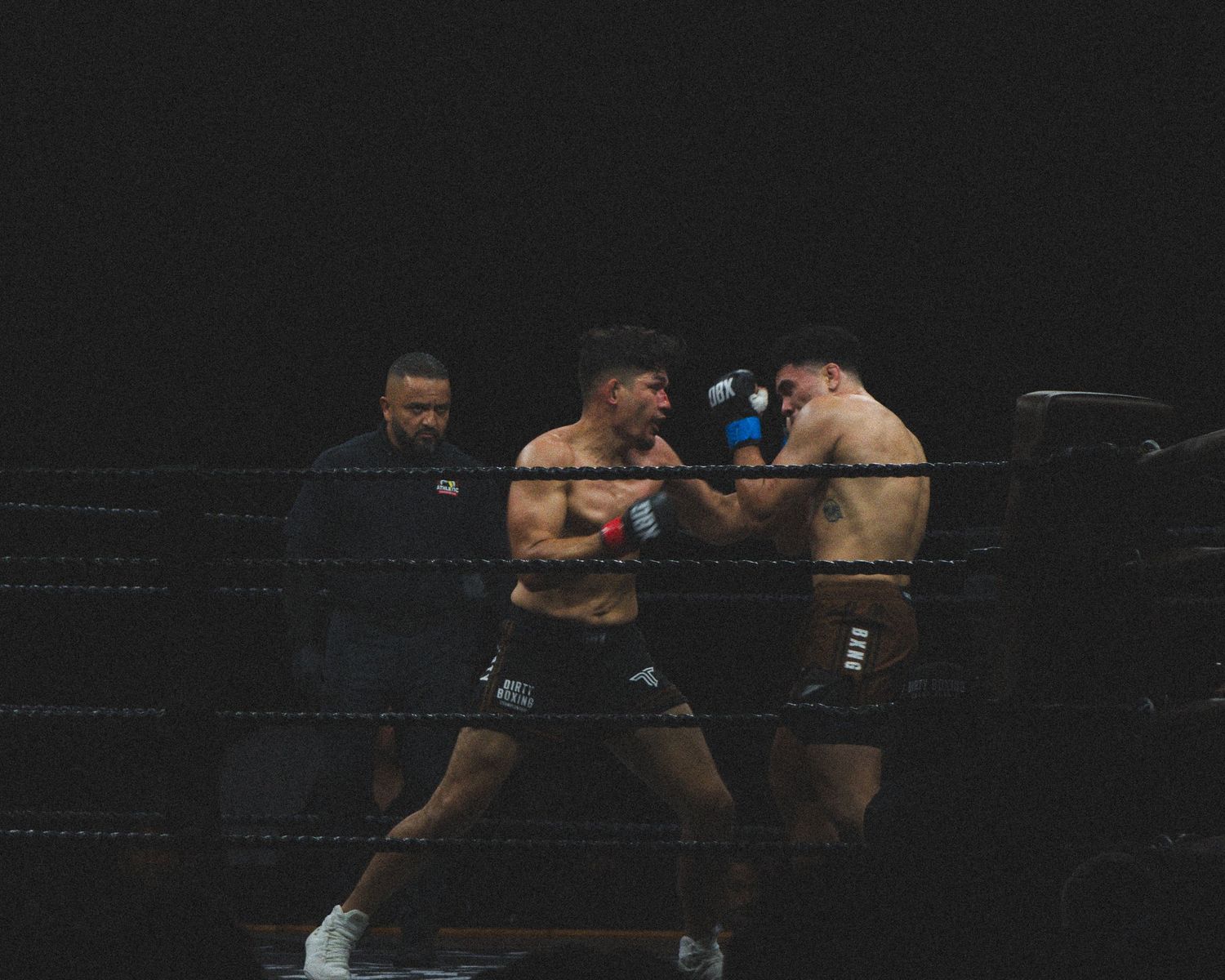 Boxers trade punches during a competitive match in a dark arena setting.