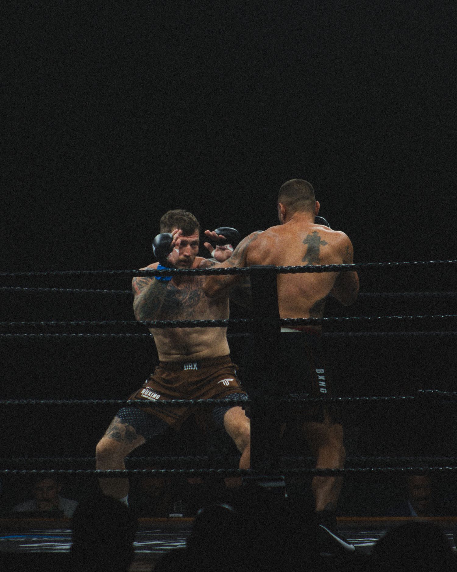 Two wrestlers exchange strikes during intense match in darkly lit professional wrestling ring.