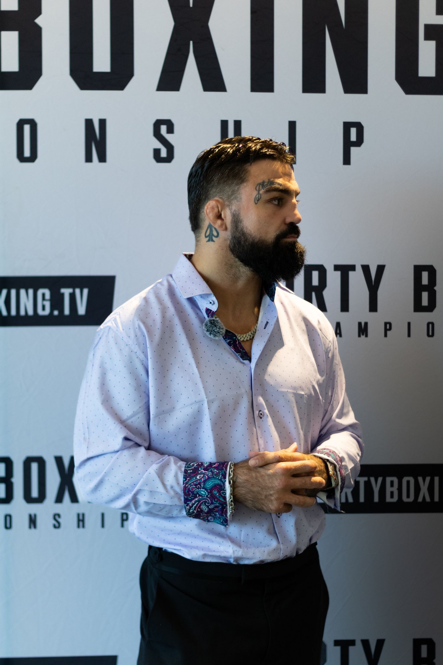Man in white shirt gestures animatedly during interview against Dirty Boxing Championship backdrop.