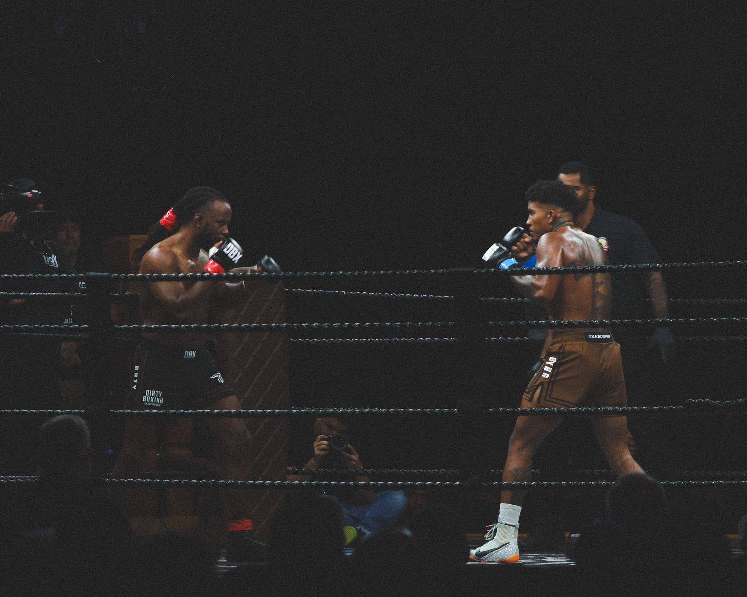 Two boxers square off in a professional boxing match under dramatic lighting conditions.