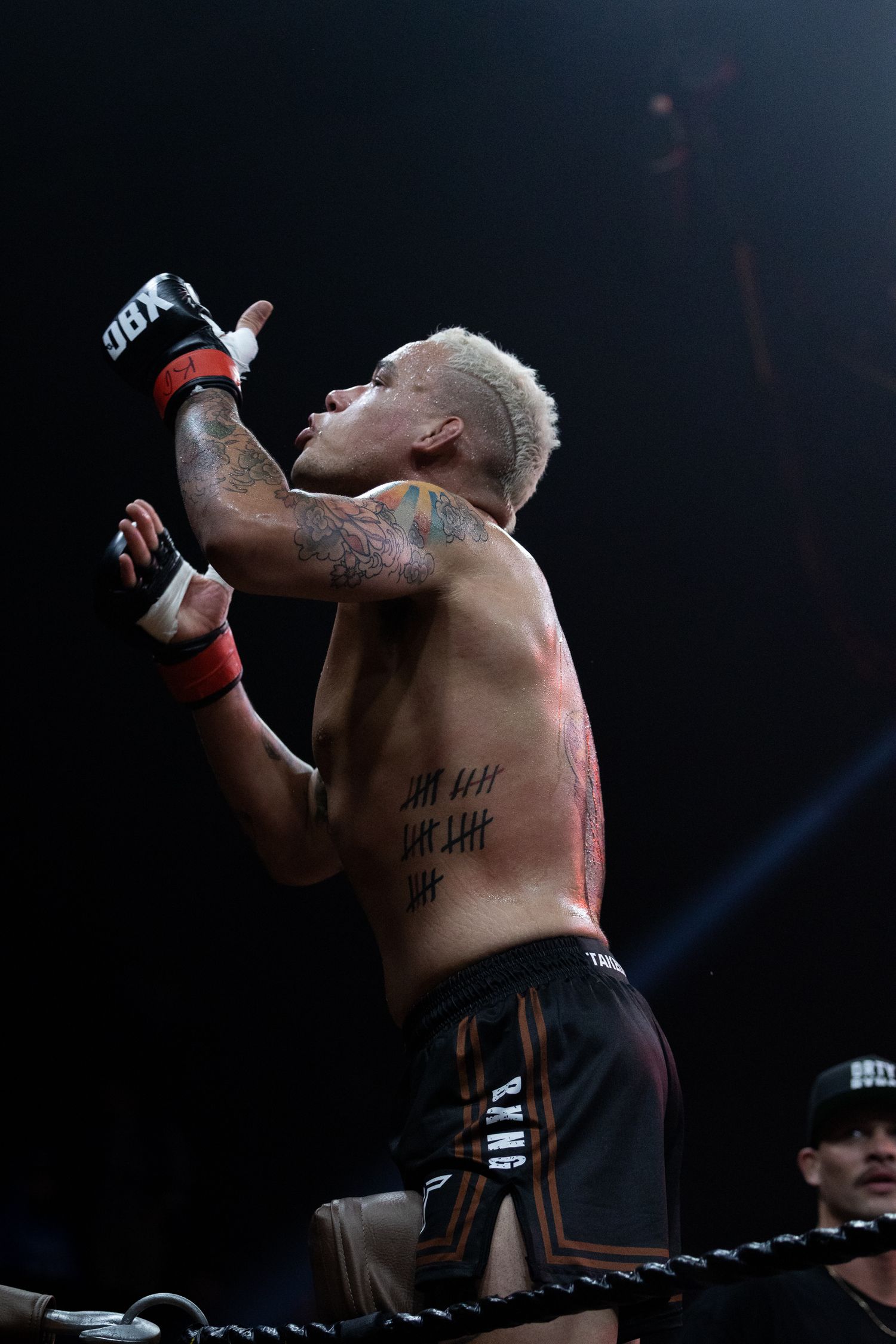 A shirtless fighter celebrates with arms raised in a darkened arena.