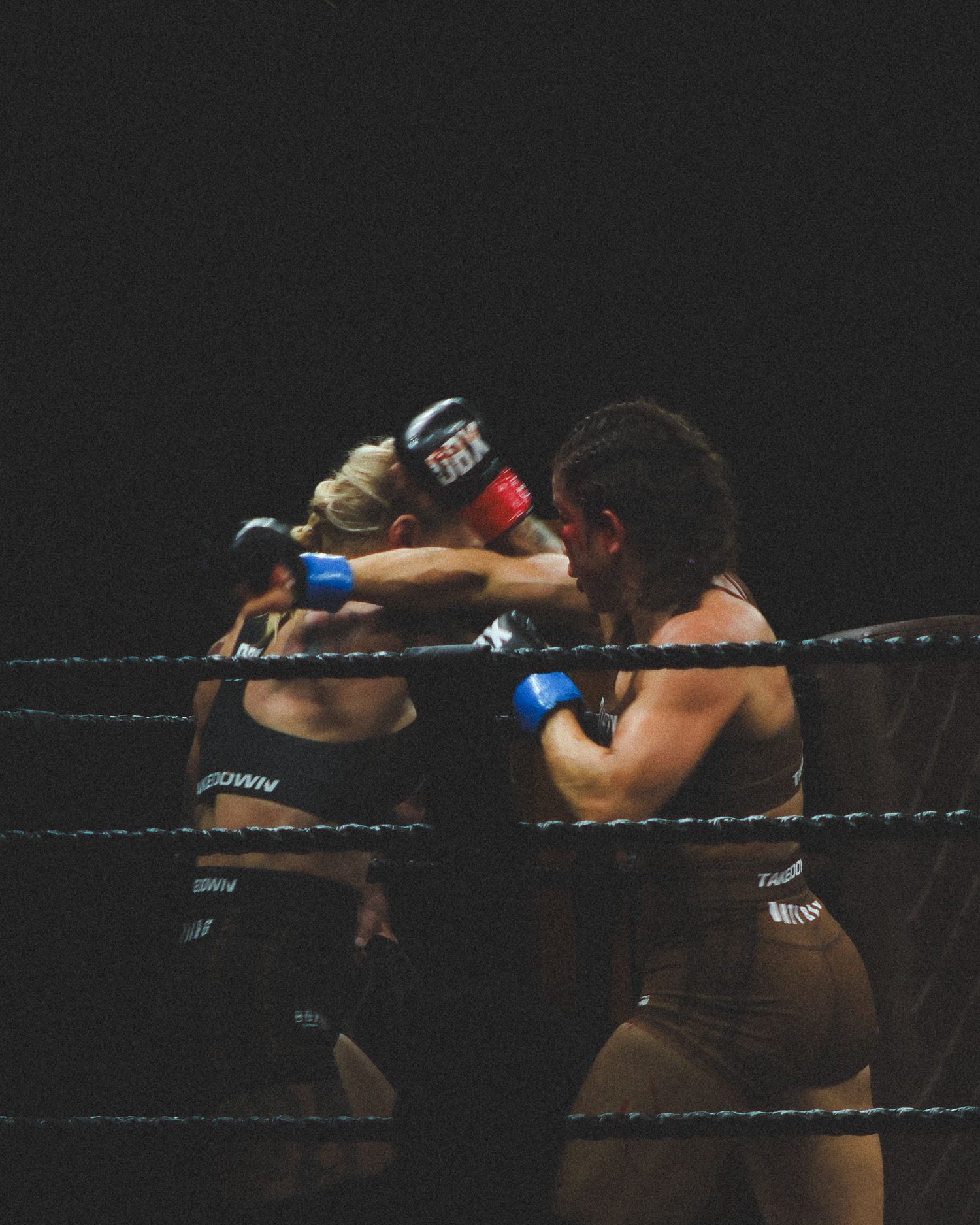 Boxers trade blows in a professional wrestling ring with dramatic lighting.