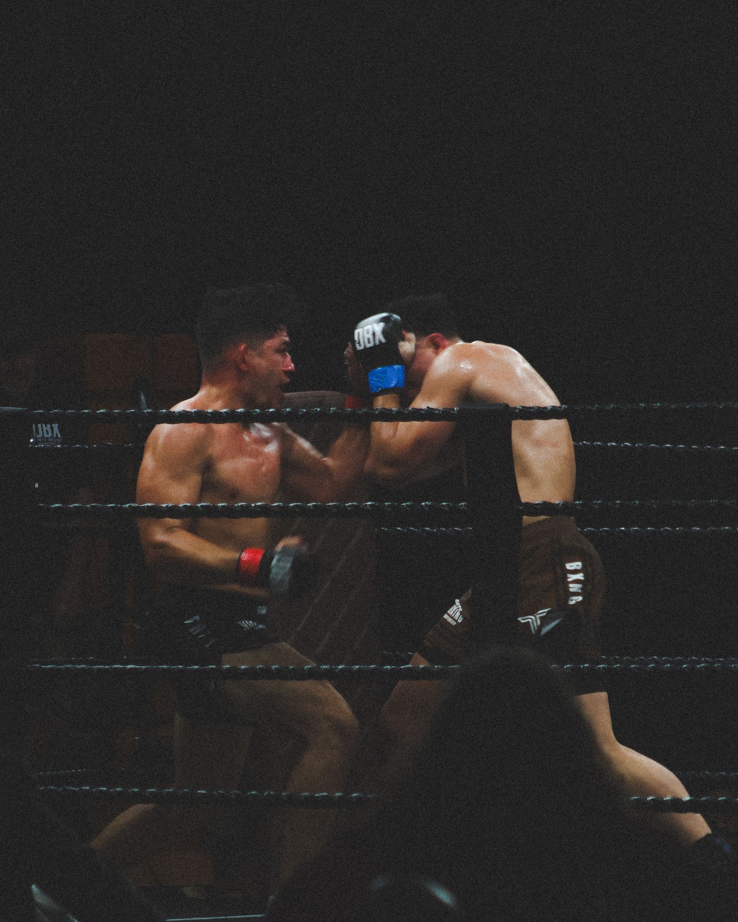 Two MMA fighters exchange blows during an intense match in a darkened arena.