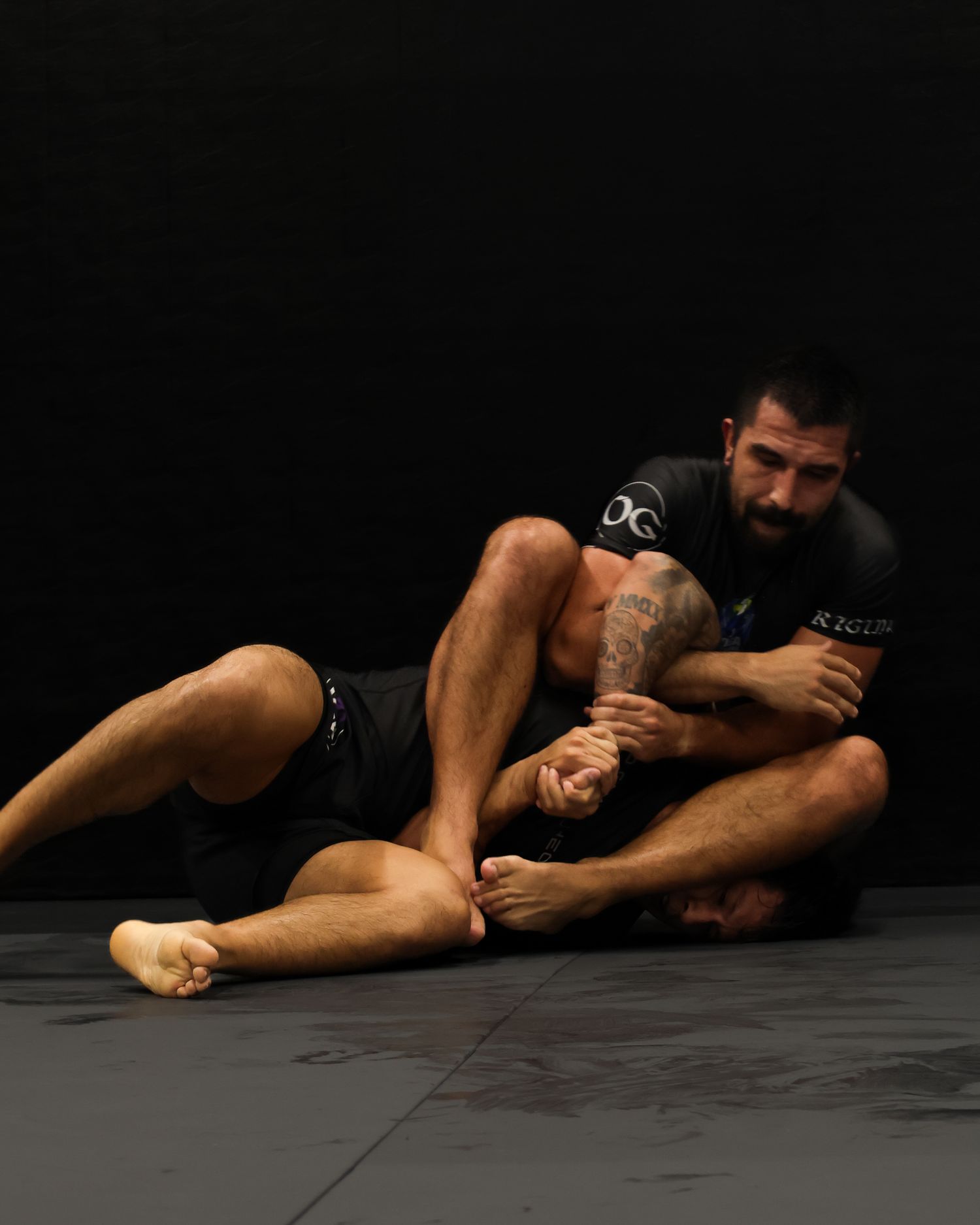 Martial artists practicing grappling techniques on black mat during training session.