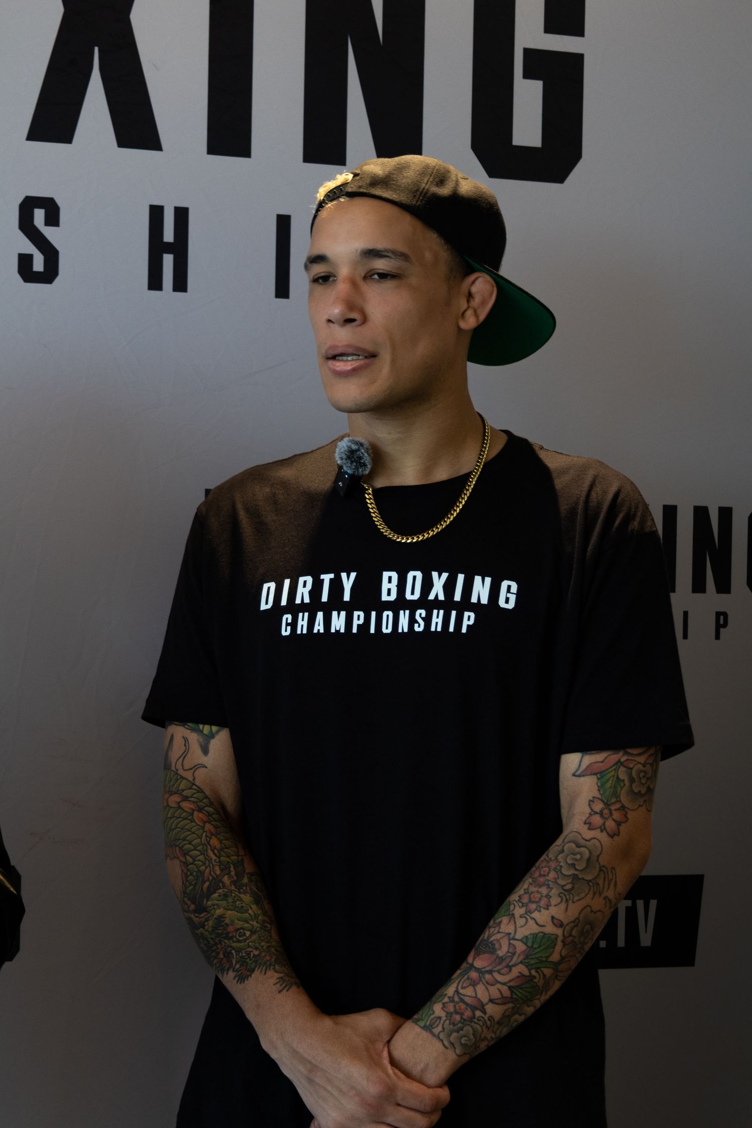 Person in black Dirty Boxing shirt with tattoos smiles during promotional event.