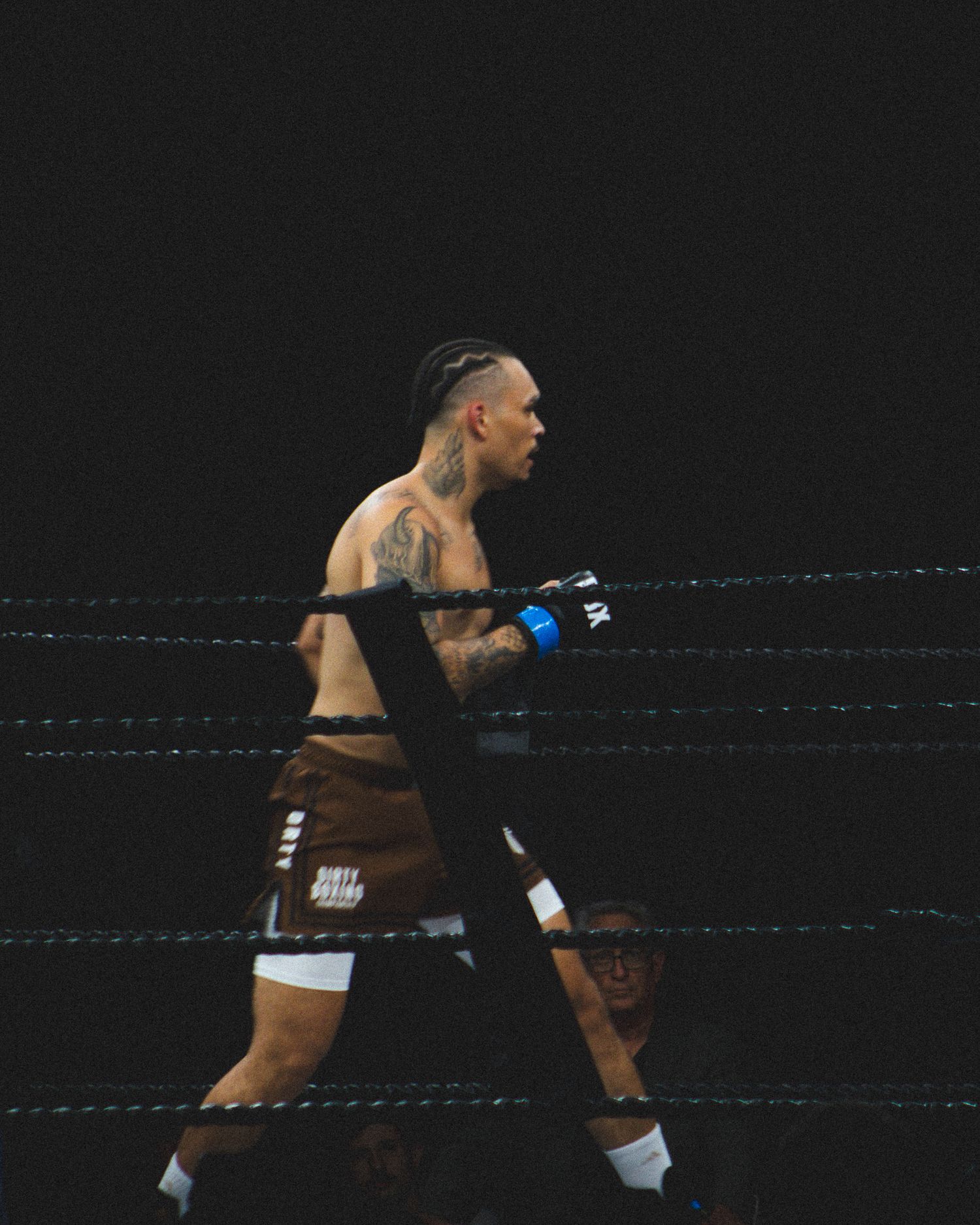 A tattooed boxer in black shorts stands ready in fighting stance during a match.